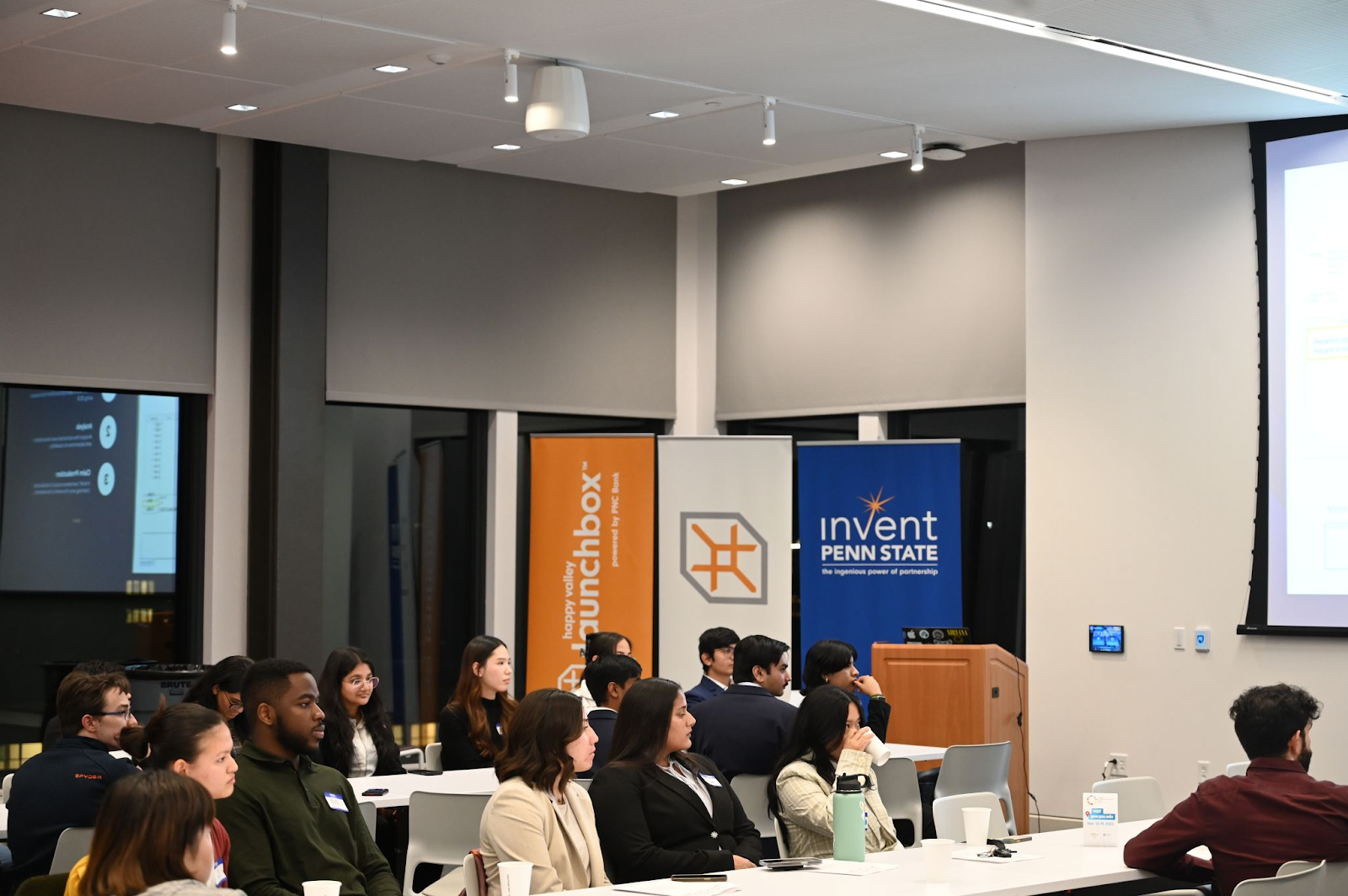 Students sitting at rows of tables during pitch competition