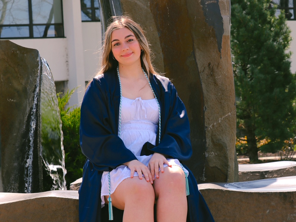 Sam Hagenbush wearing graduation cap sitting in front of fountain