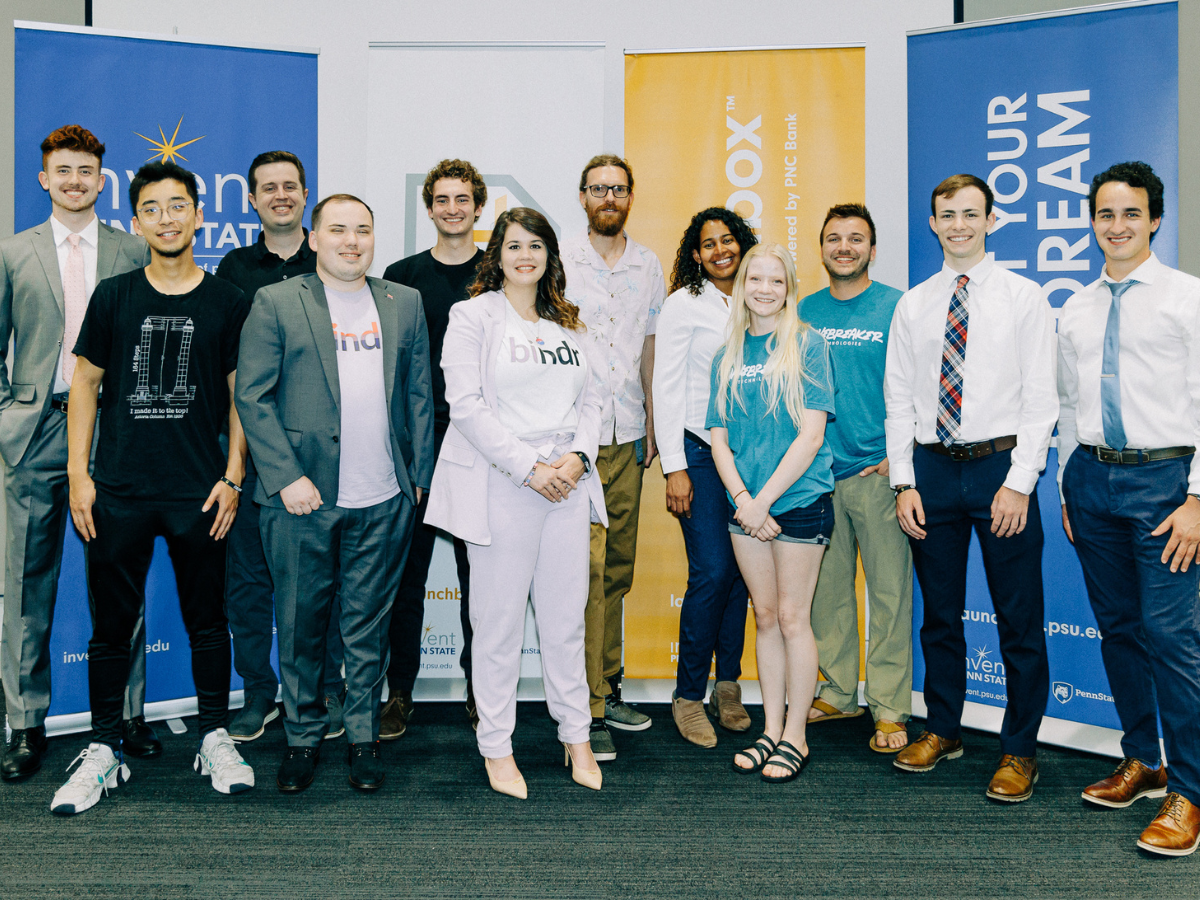 12 students pose standing for photo in front of Invent Penn State signage