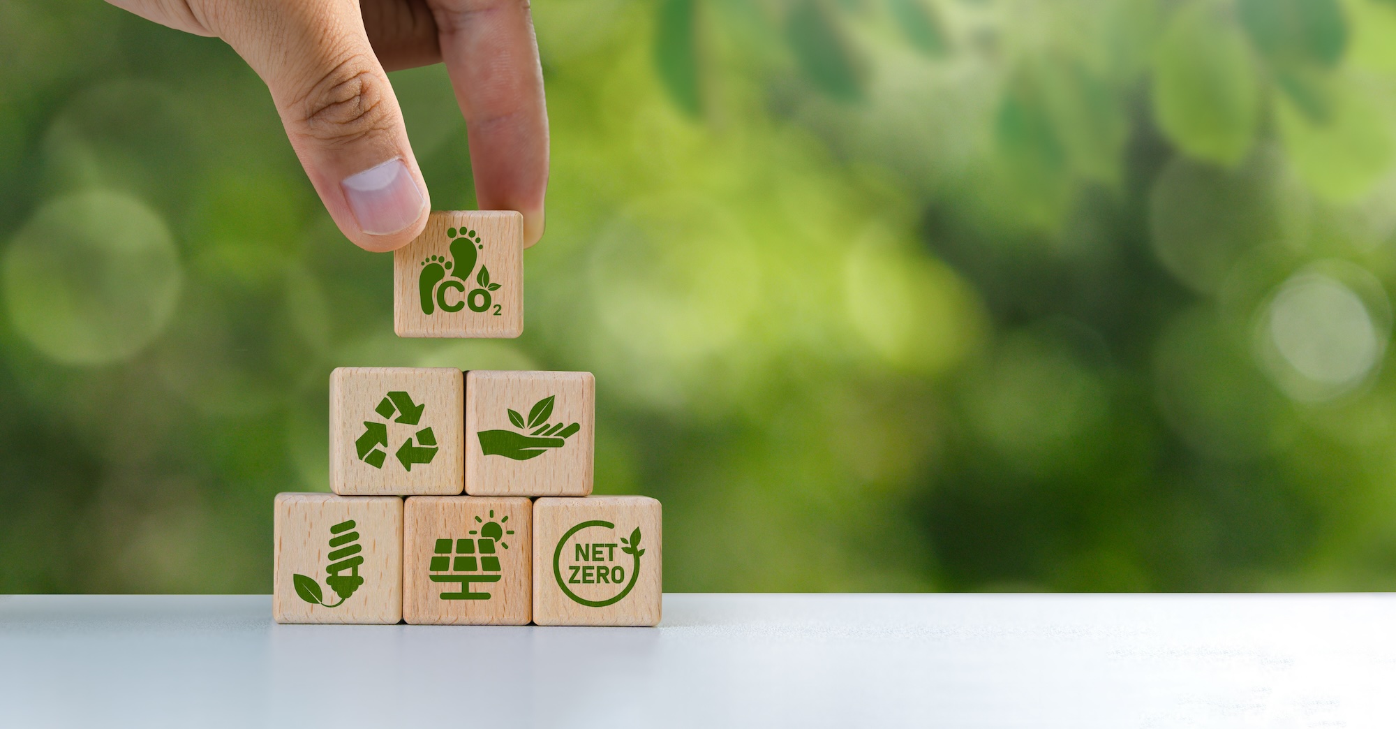 Stock image of person stacking wooden blocks decorated with green-energy icons.