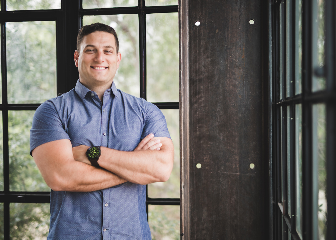 Mike Levkulich stands with his arms crossed in front of a large vertical window.