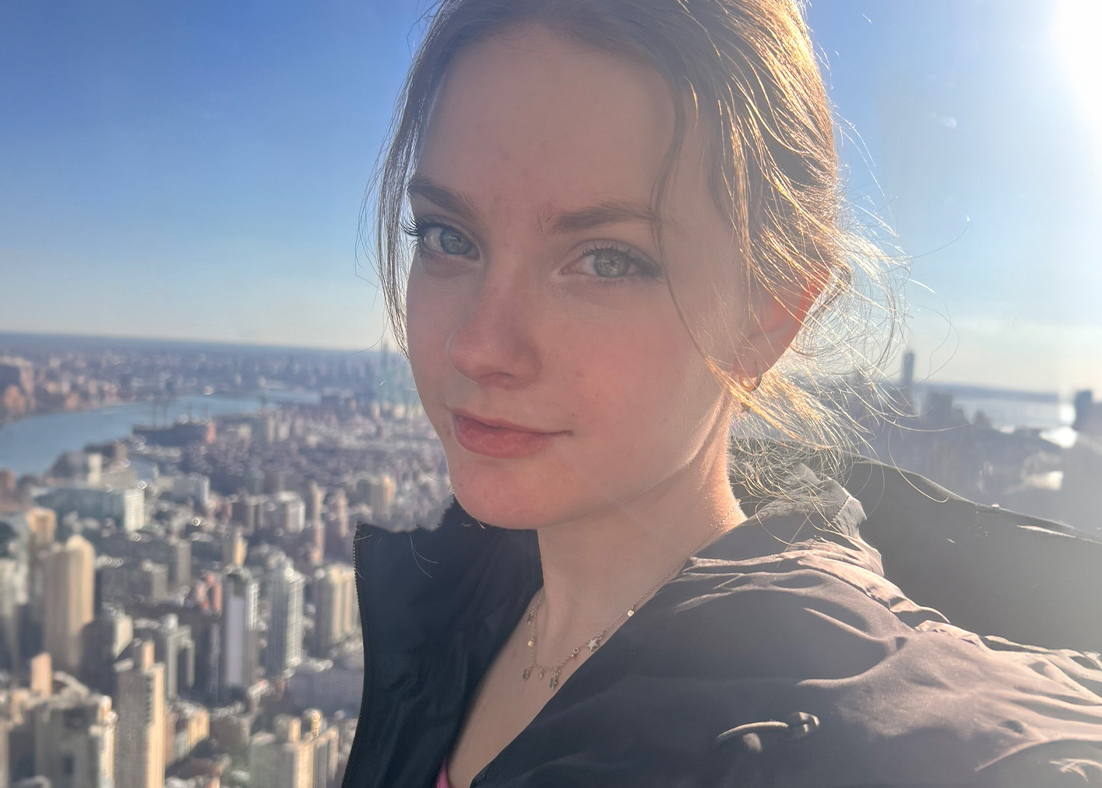 A selfie of Johnna D’Ecclesiis with a high-rise view of a city in the background.