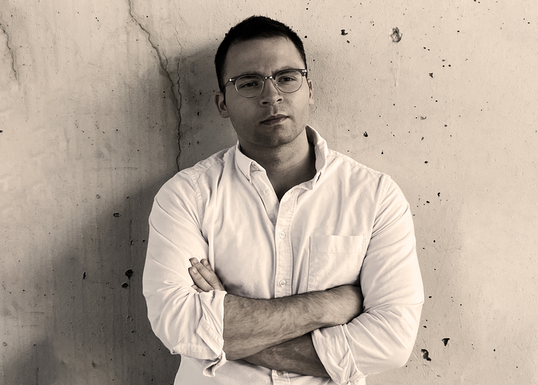 A black and white photograph of Dillon Brown leaning against a wall. 