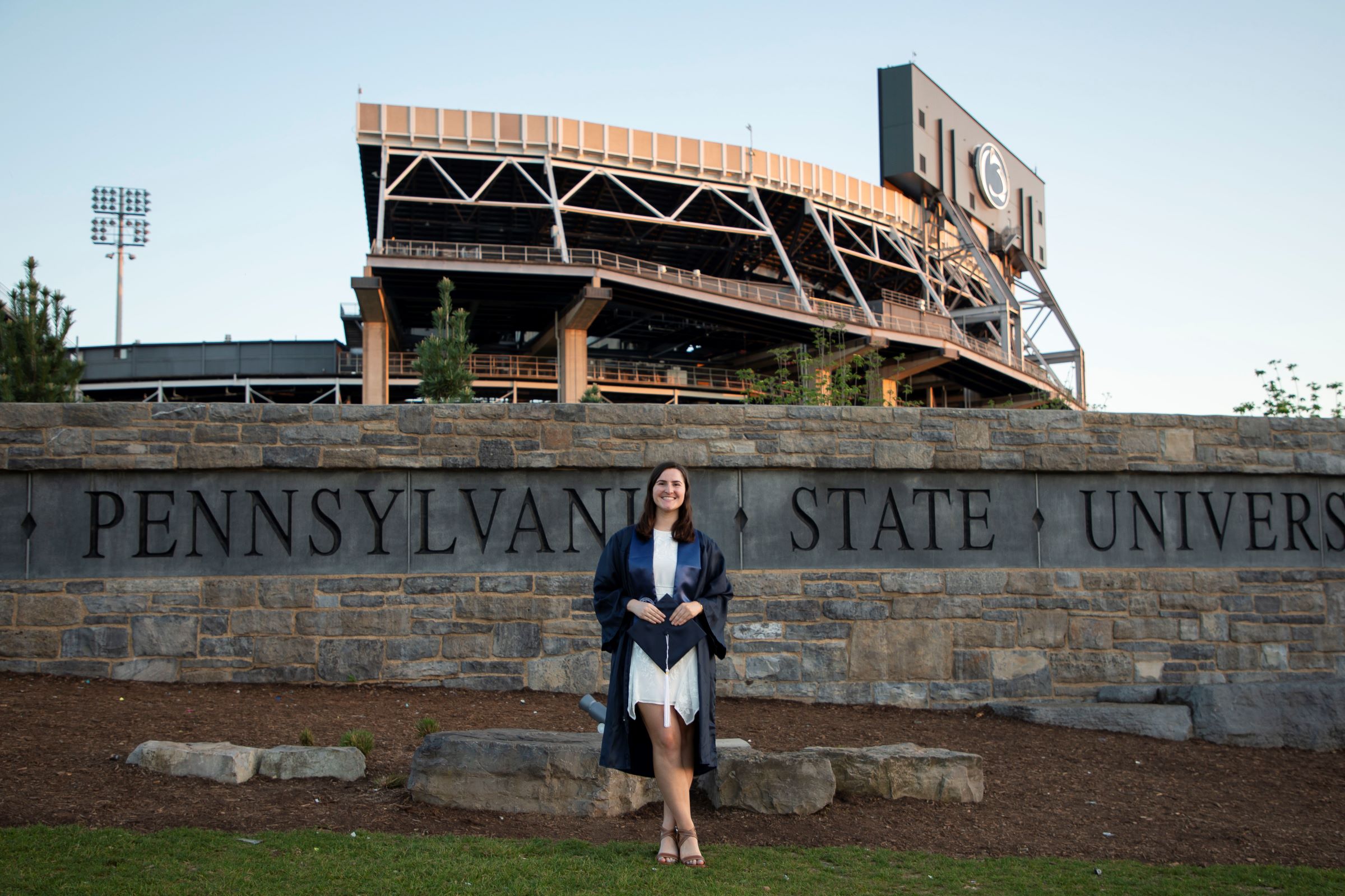 person in cap and gown in front of sports stadium