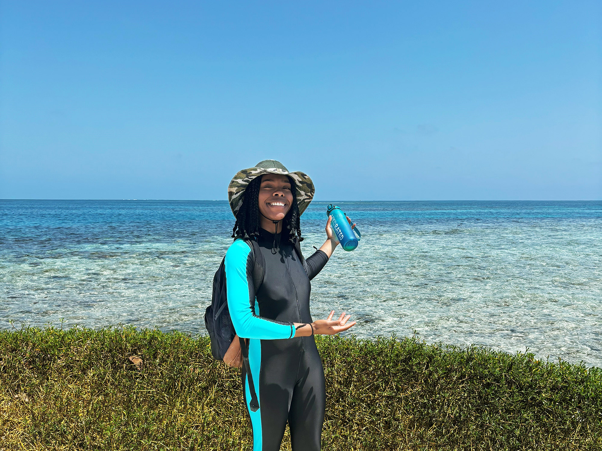 a woman points to the ocean with seaweed in the immediate background