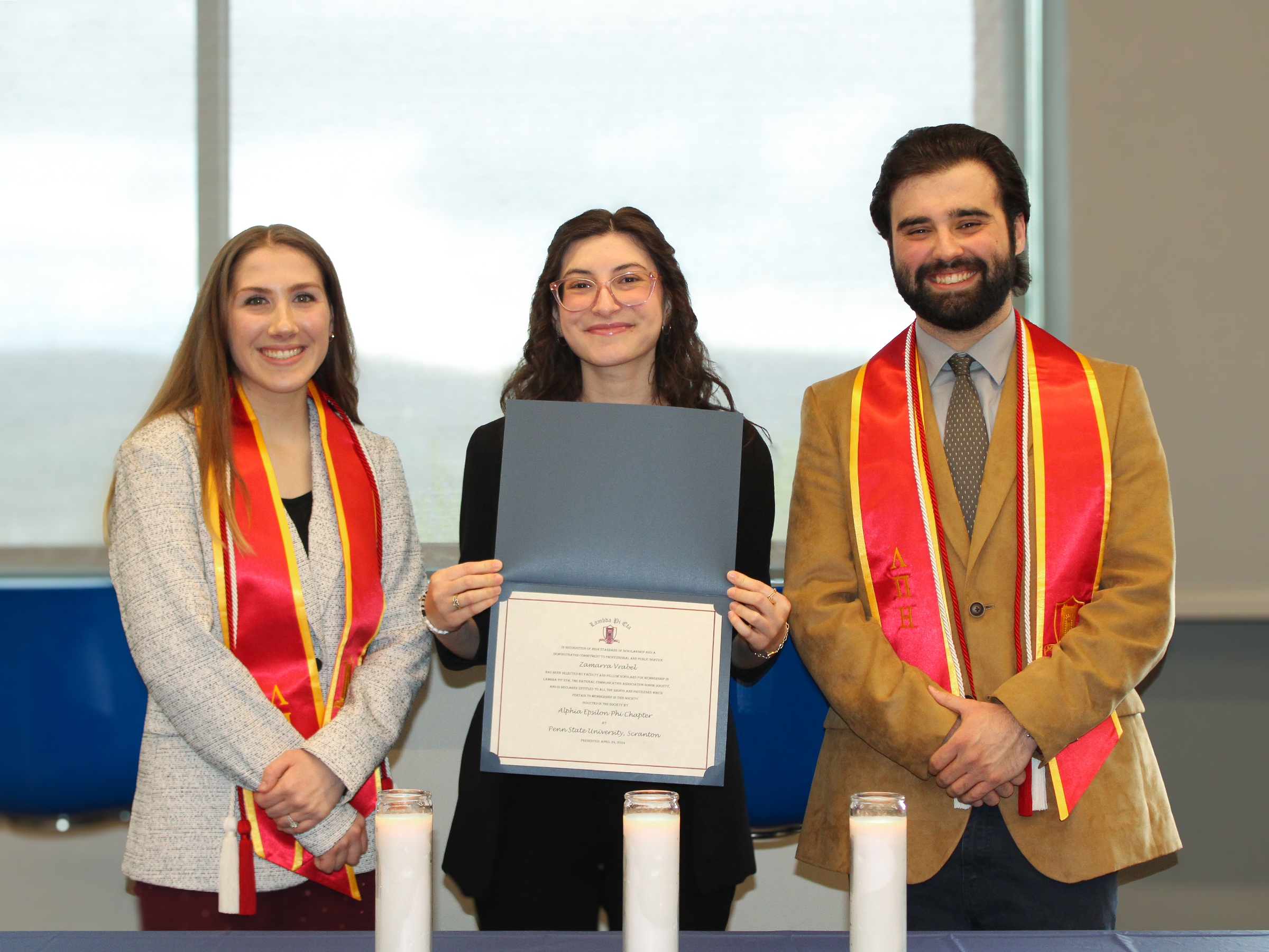 New lambda pi eta members pose with their certificates and graduation cords