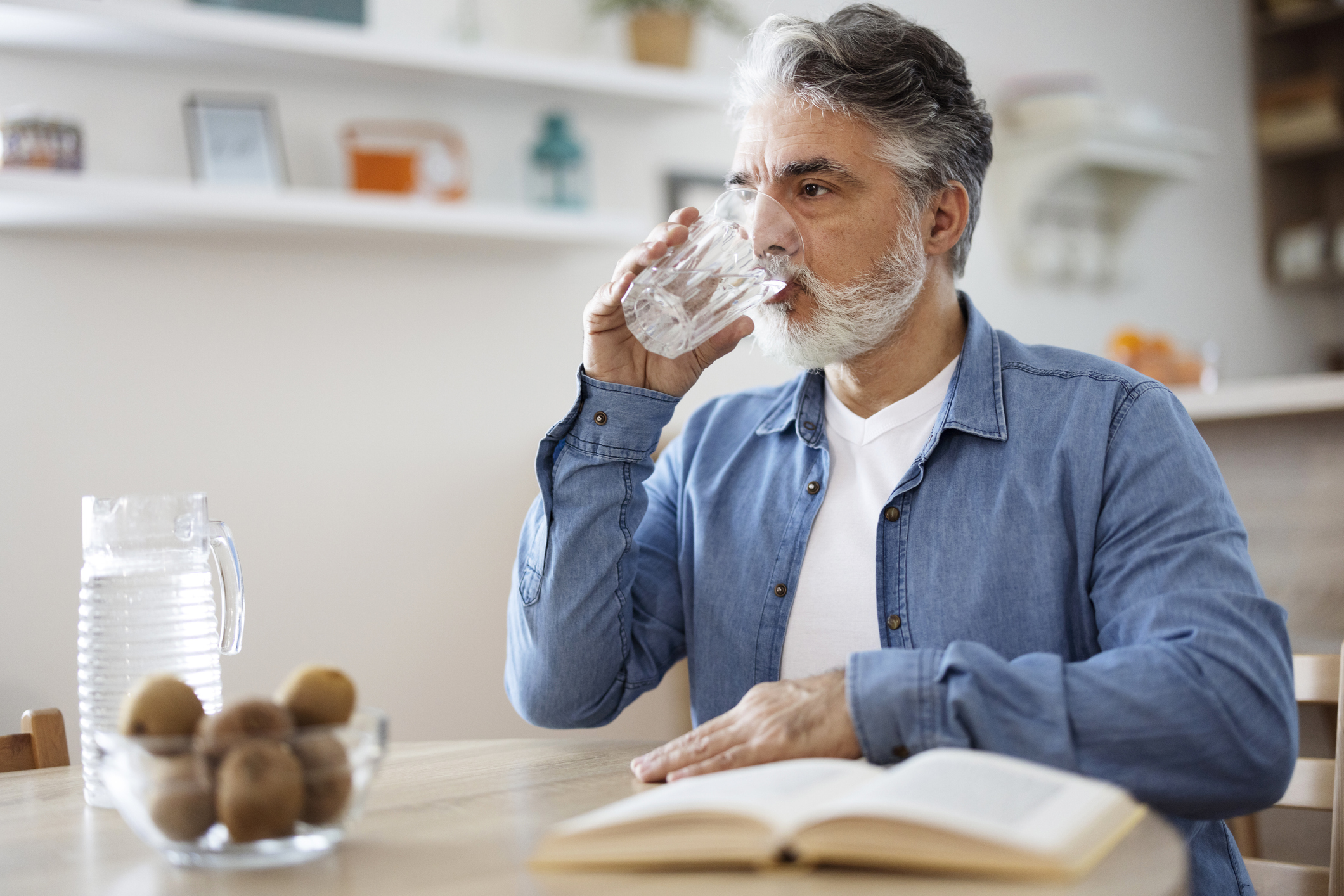 Older person sitting in a kitchen drinking water