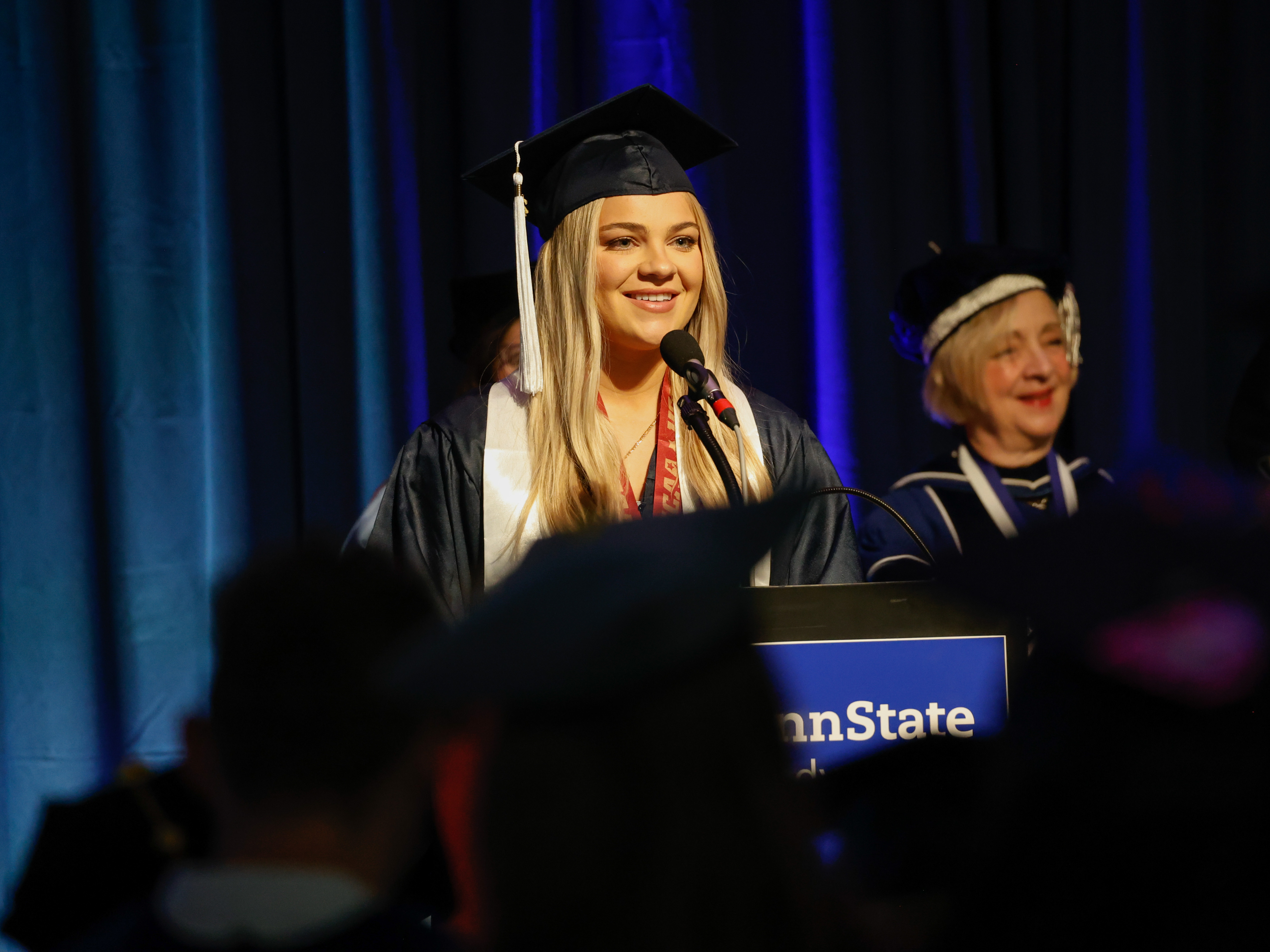 A person wearing a graduation gown stands at a lectern to speak at commencement.