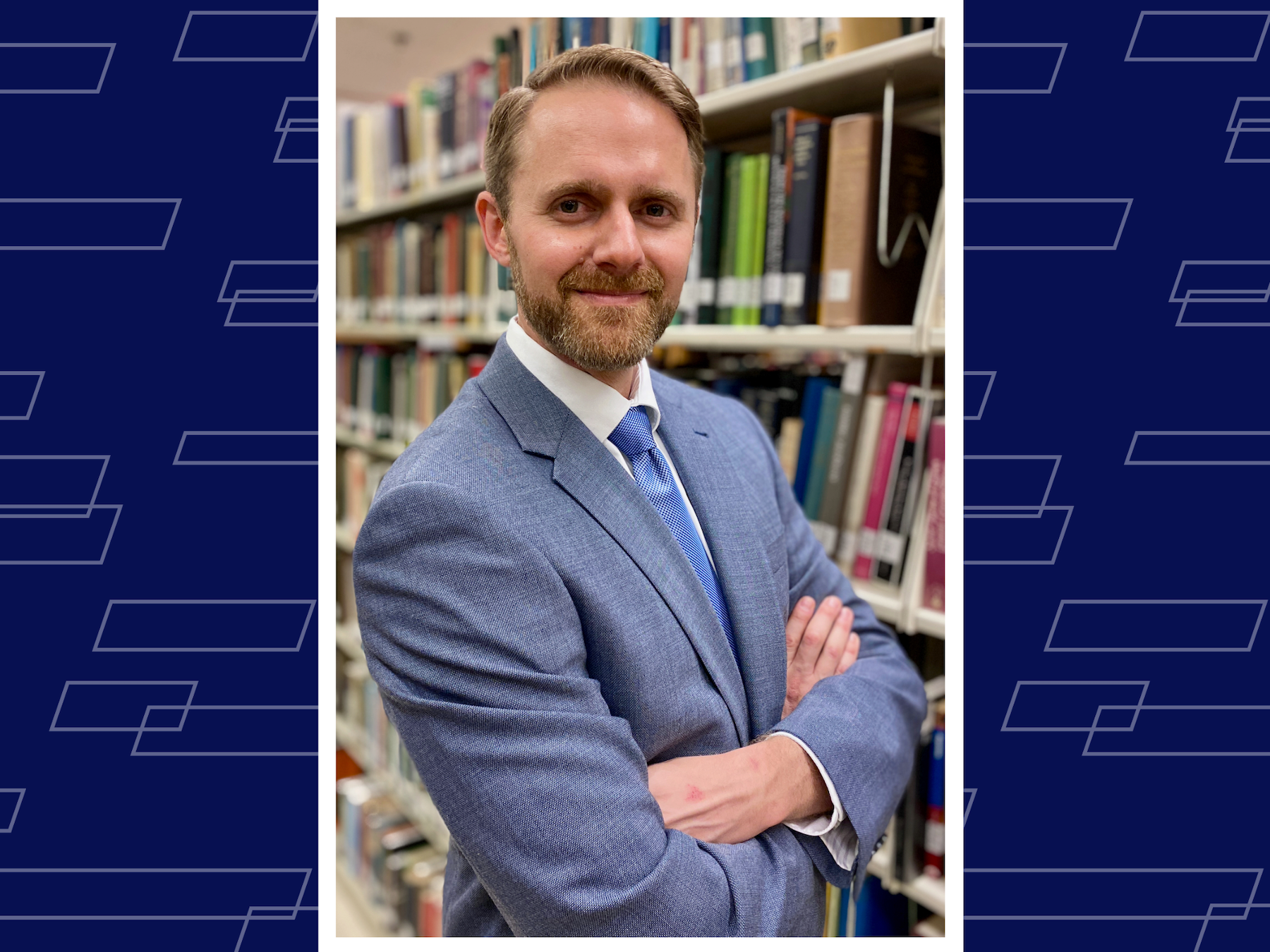 smiling person in suit and tie crossing arms standing in front of tall full bookshelf