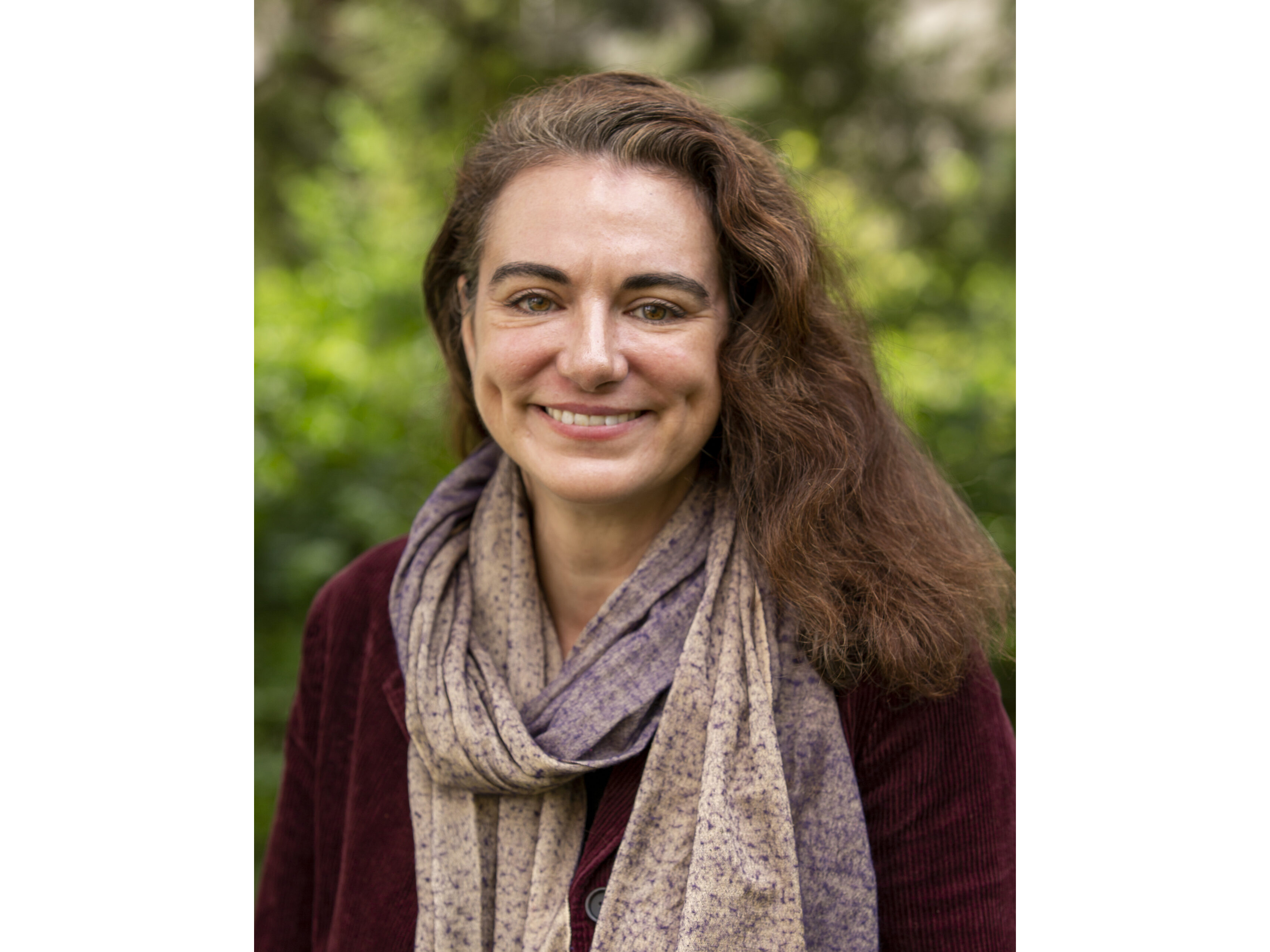 Sarah Brothers head shot with long wavy brown hair, smiling, purple print scarf and maroon jacket.