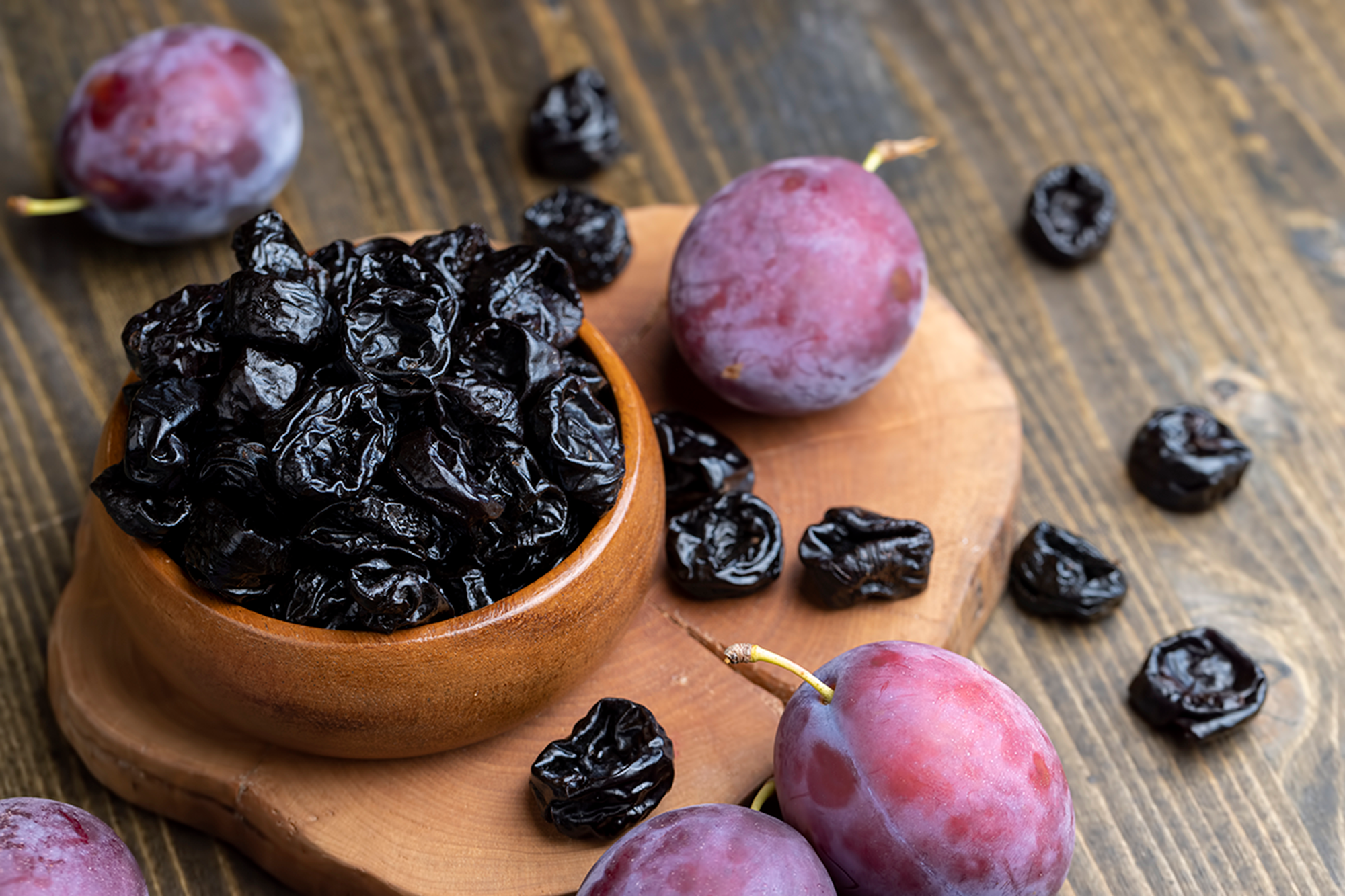 a pile of dried prunes and fresh plums on a wooden table