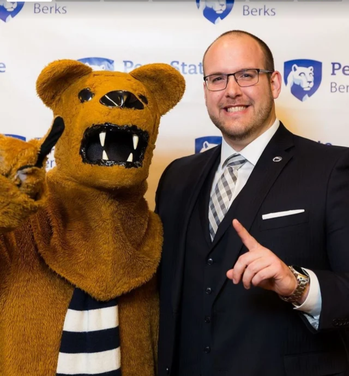 A person stands with the Nittany Lion, both hold up their index fingers