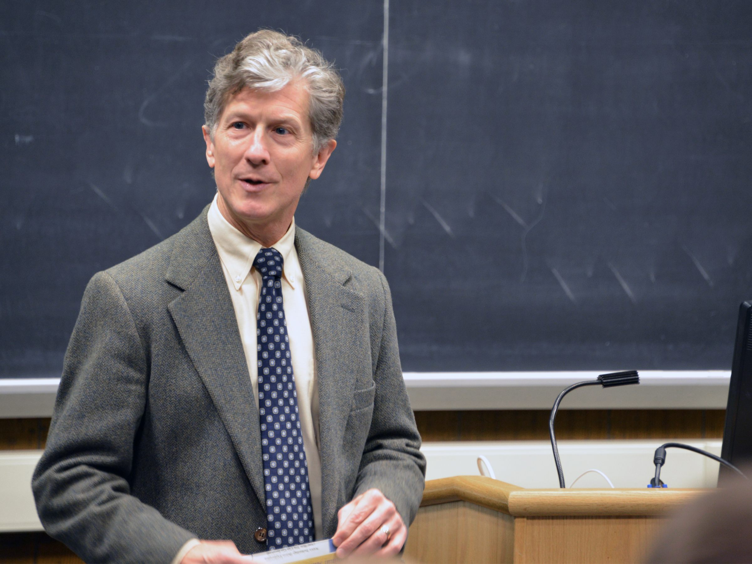 An individual wearing a suit and tie stands in front of a blackboard.