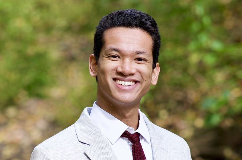 Young college-aged man with dark hair wearing a khaki suit. 