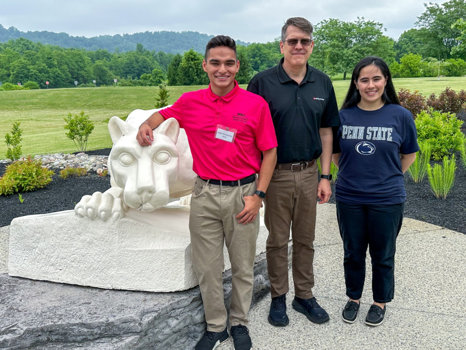 3 adults smile in front of a lion shrine 