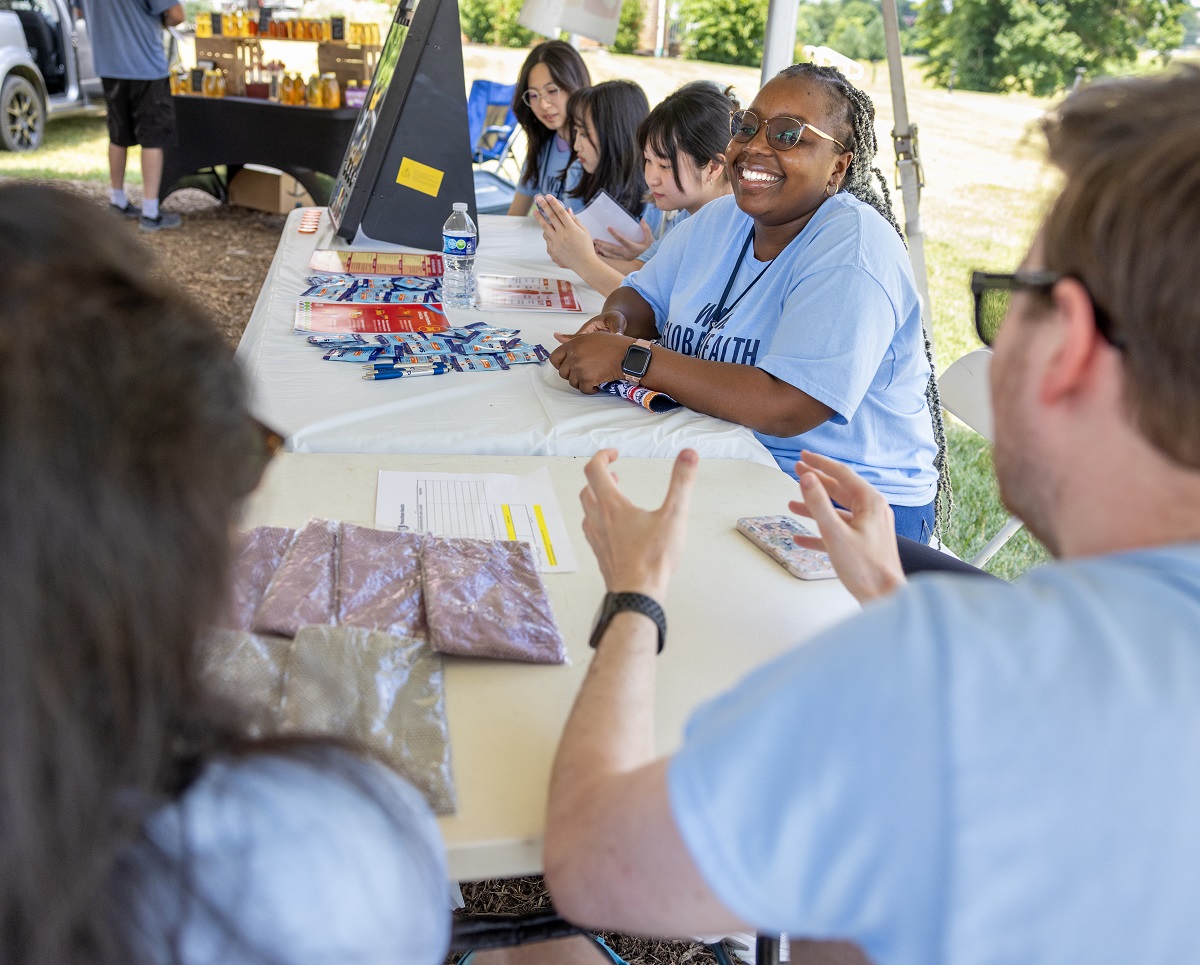 A group of students with matching shirts sit at a stand at a farmer's market