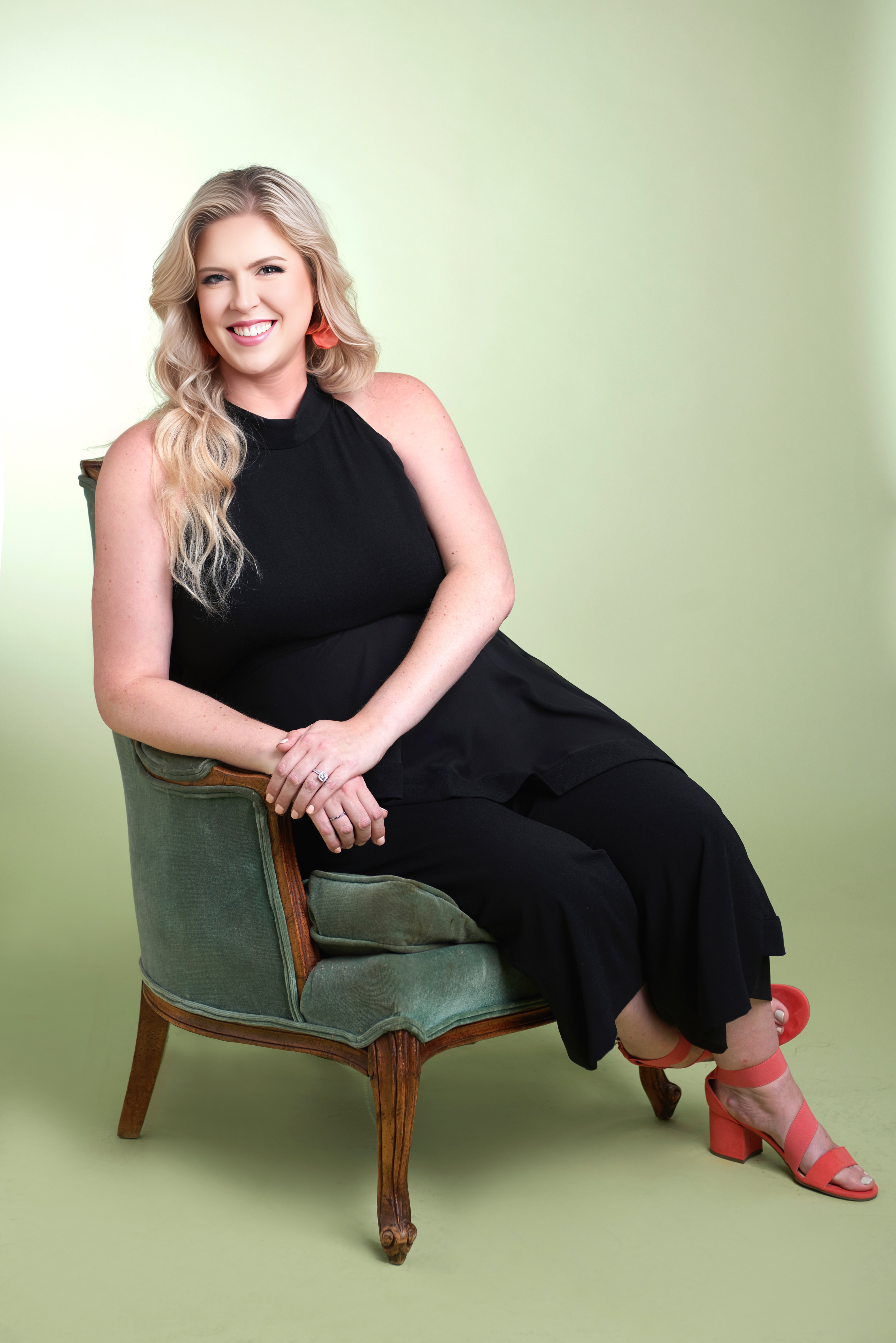 Blond woman with black dress sitting casually on a green lounge chair smiling