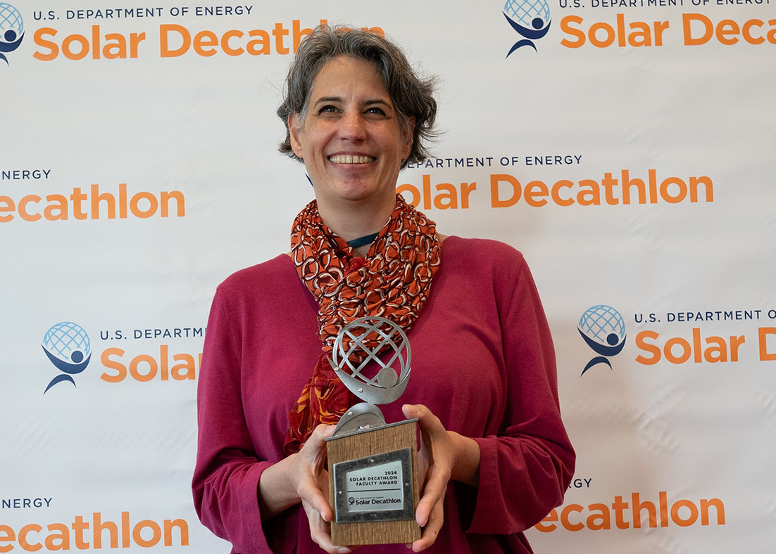 Lisa Iulo holding a trophy in front of a U.S. Department of Energy Solar Decathlon backdrop. 