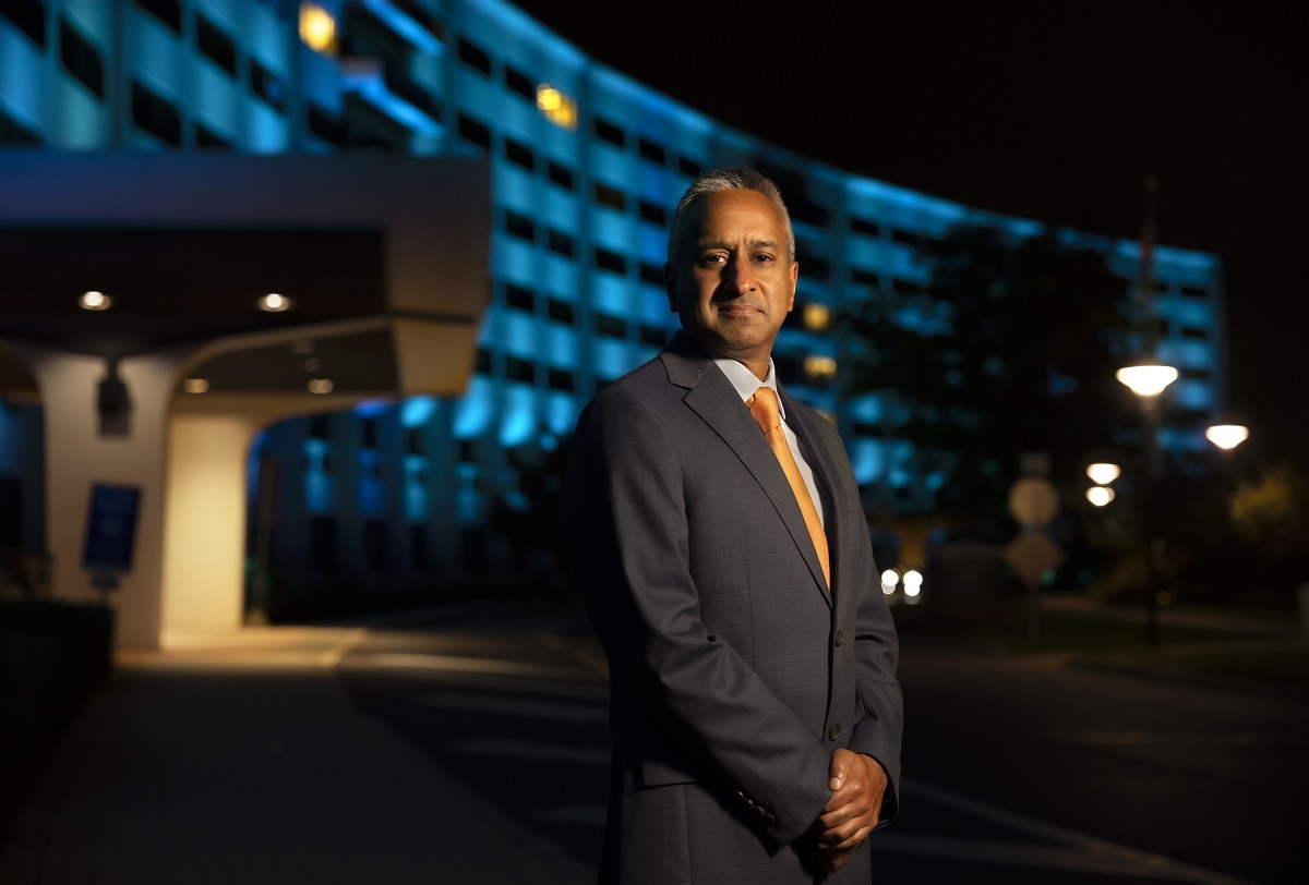 A man poses for a portrait in front of a building. The building is illuminated in blue light.