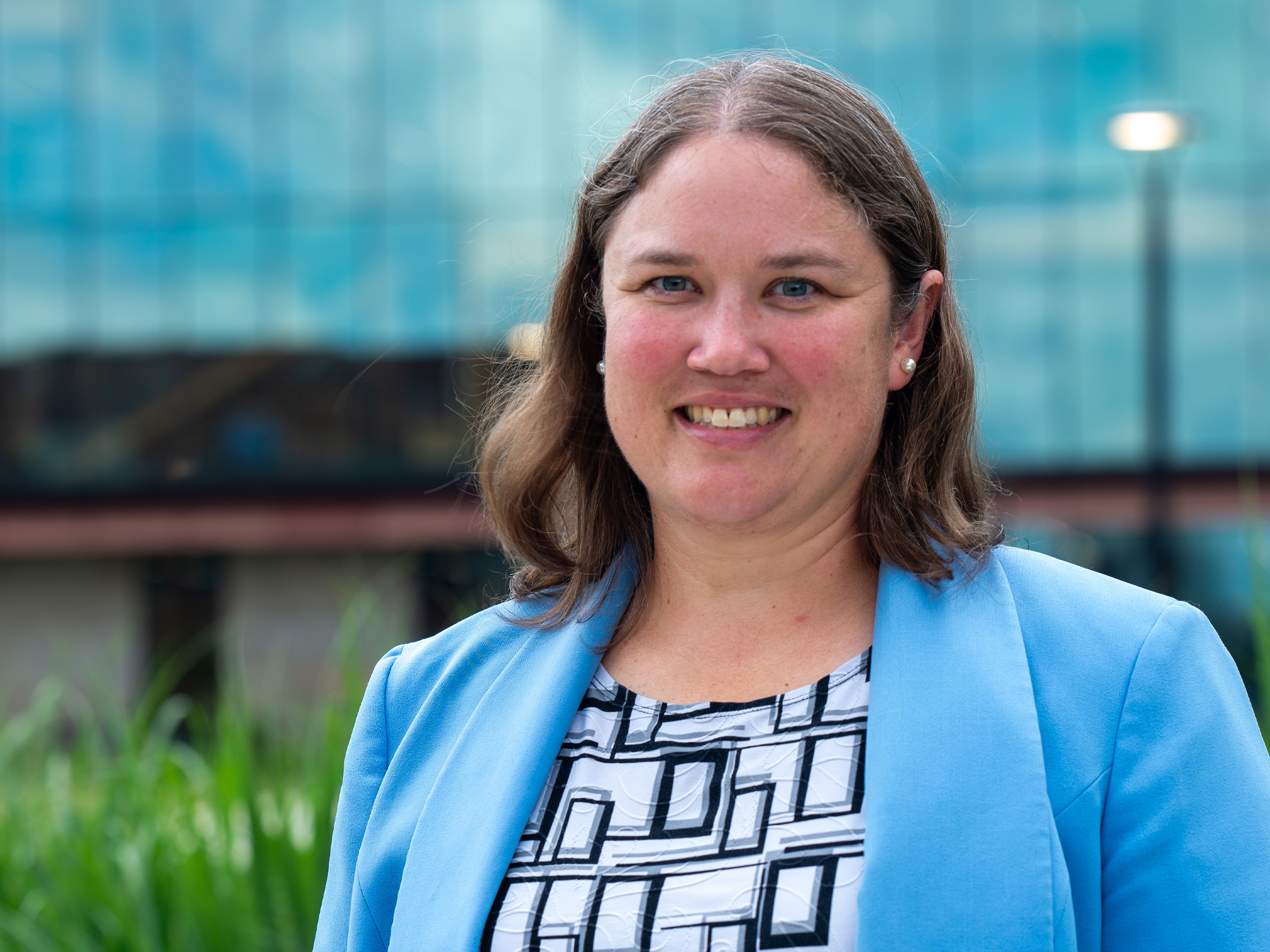 A portrait of a person in a blue blazer smiling at the camera outside. 