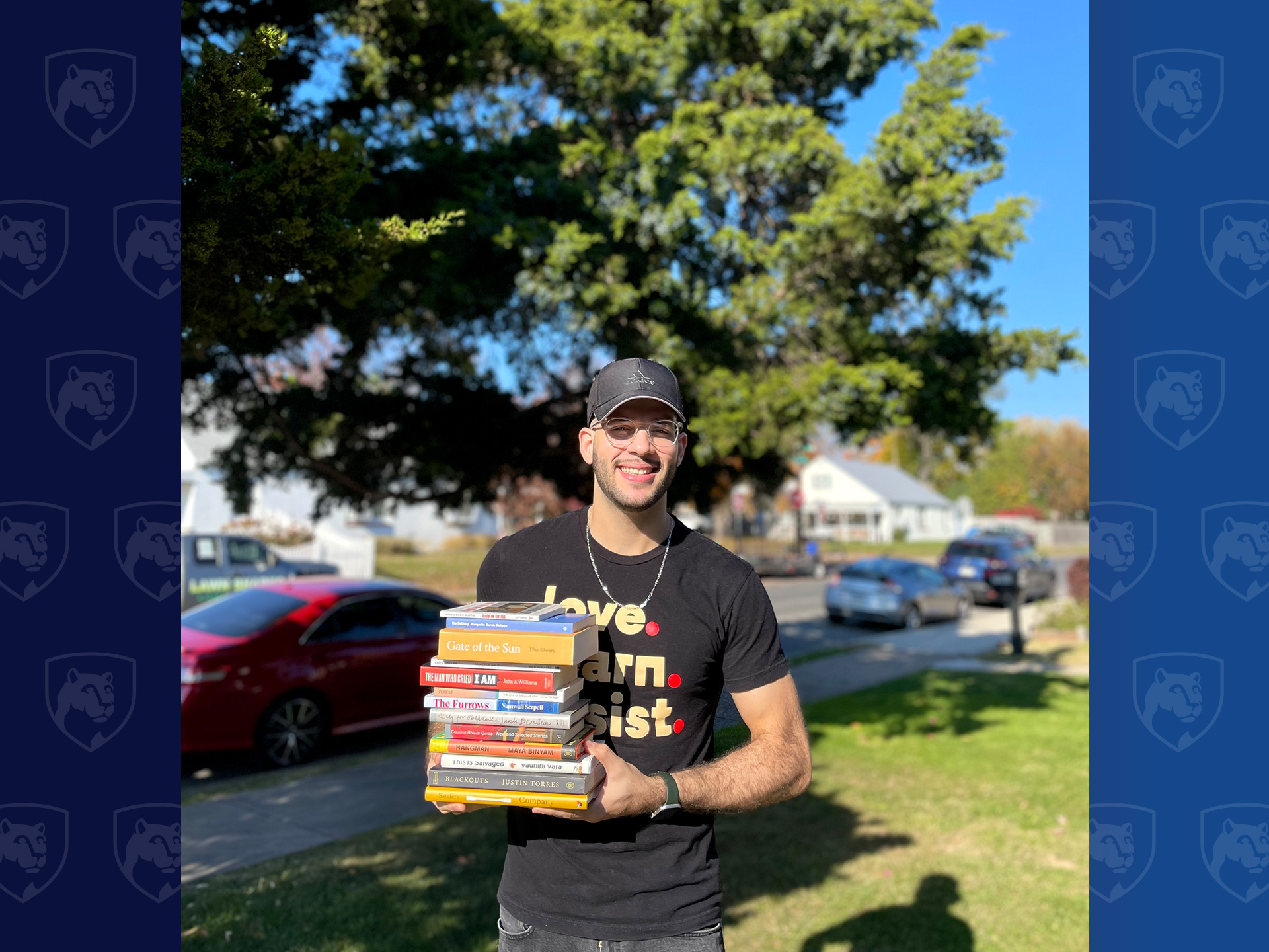 Man holding stack of books in front of a tree