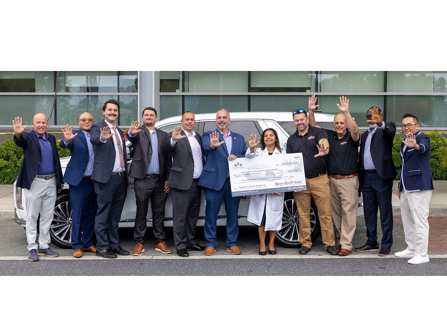 Group of people stand in front of an SUV and hold a giant check