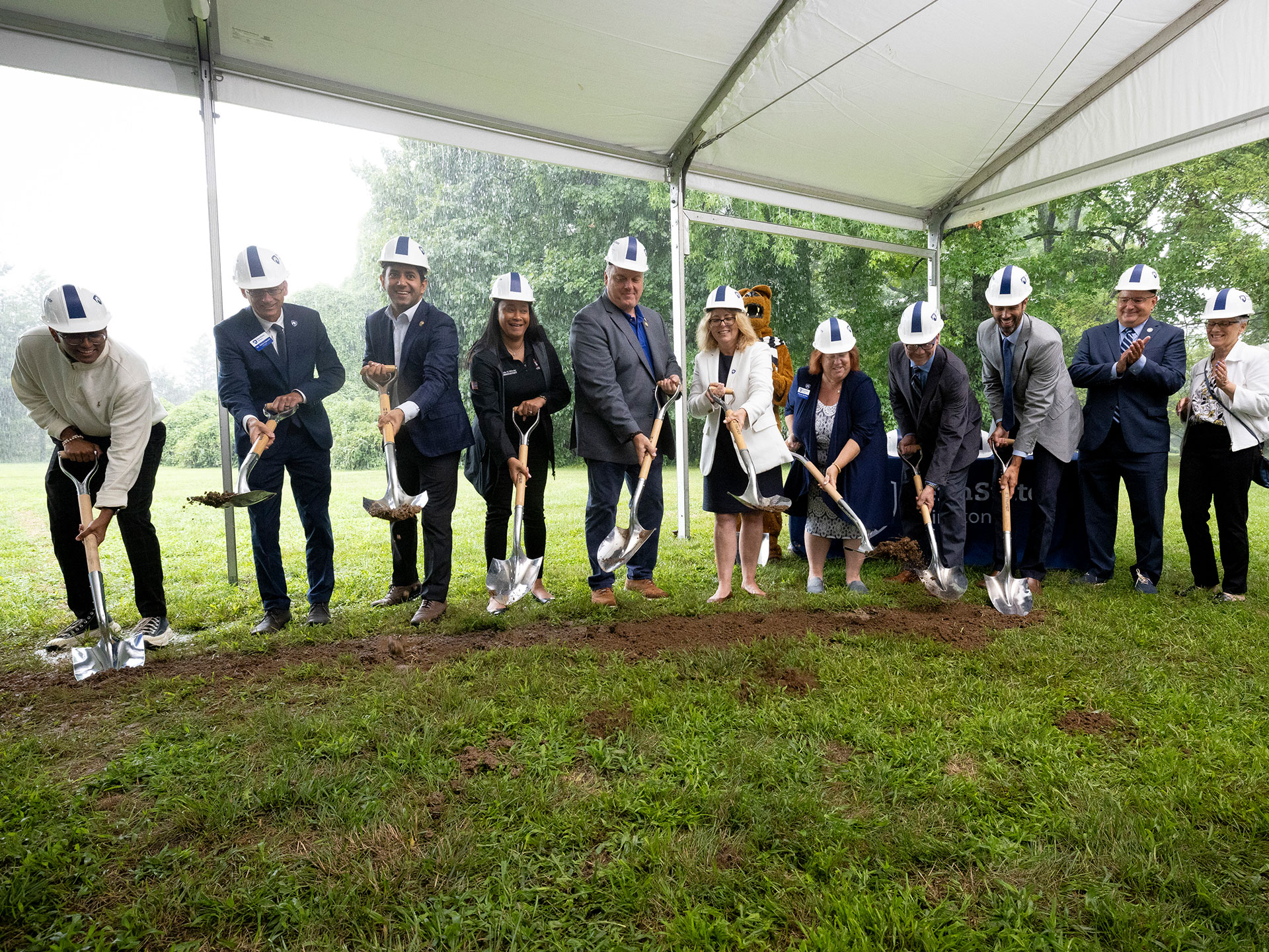 People shoveling dirt under a tent to break ground for new construction