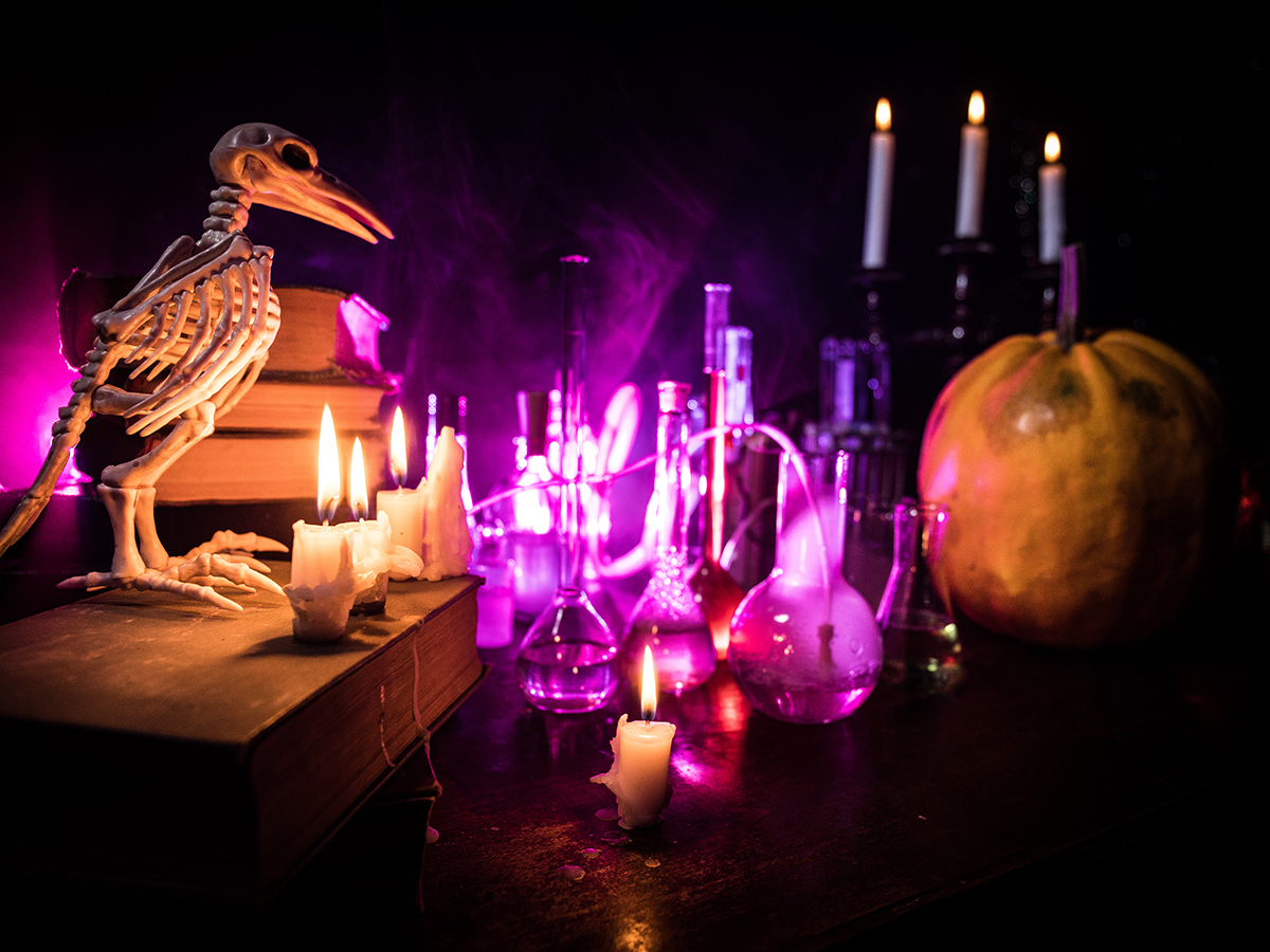 A spooky scene with a bird skeleton, glowing lab beakers, candles, and a pumpkin, set against a dark, eerie background with vibrant purple lighting.