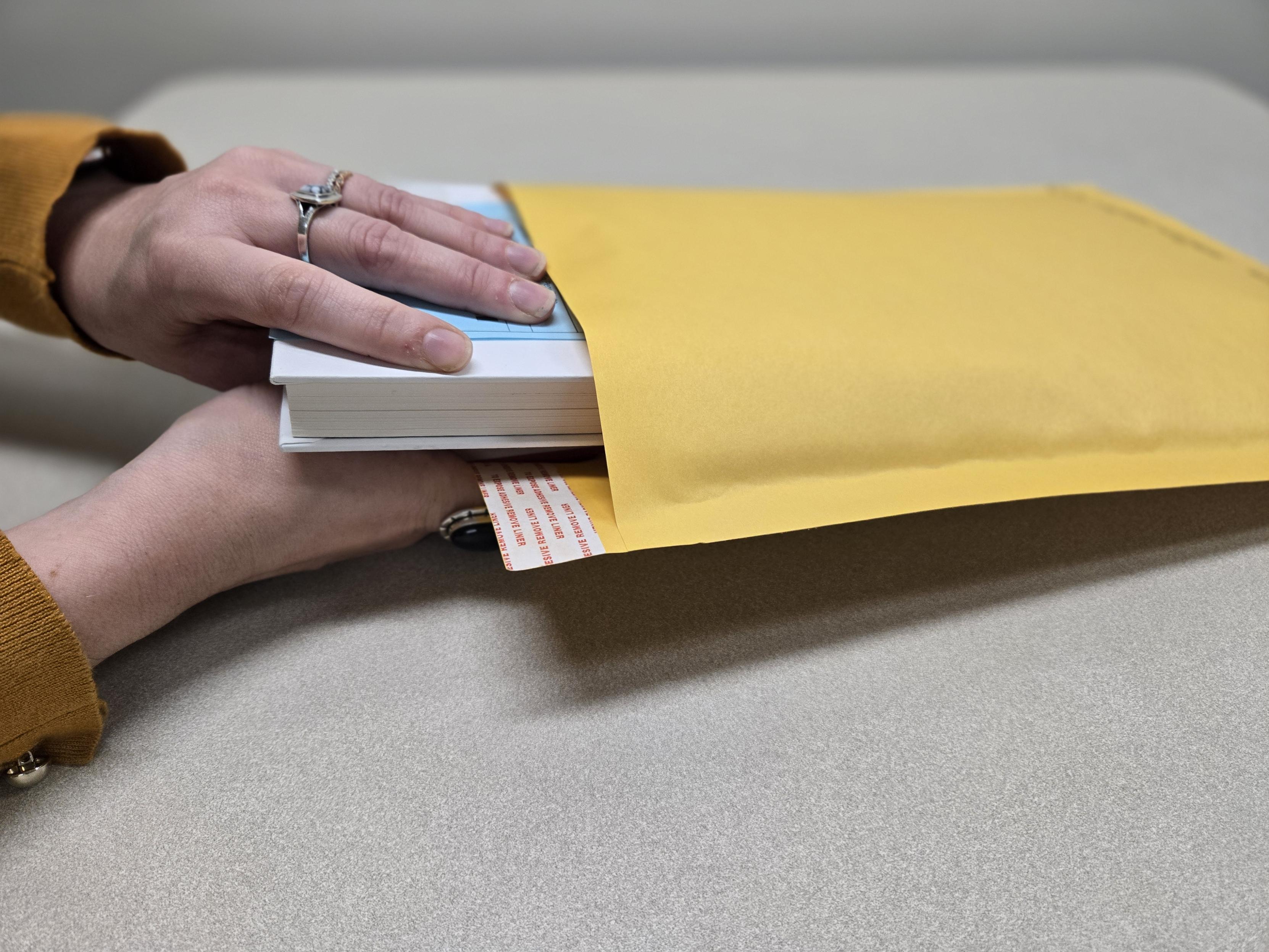 hands placing book into padded envelope