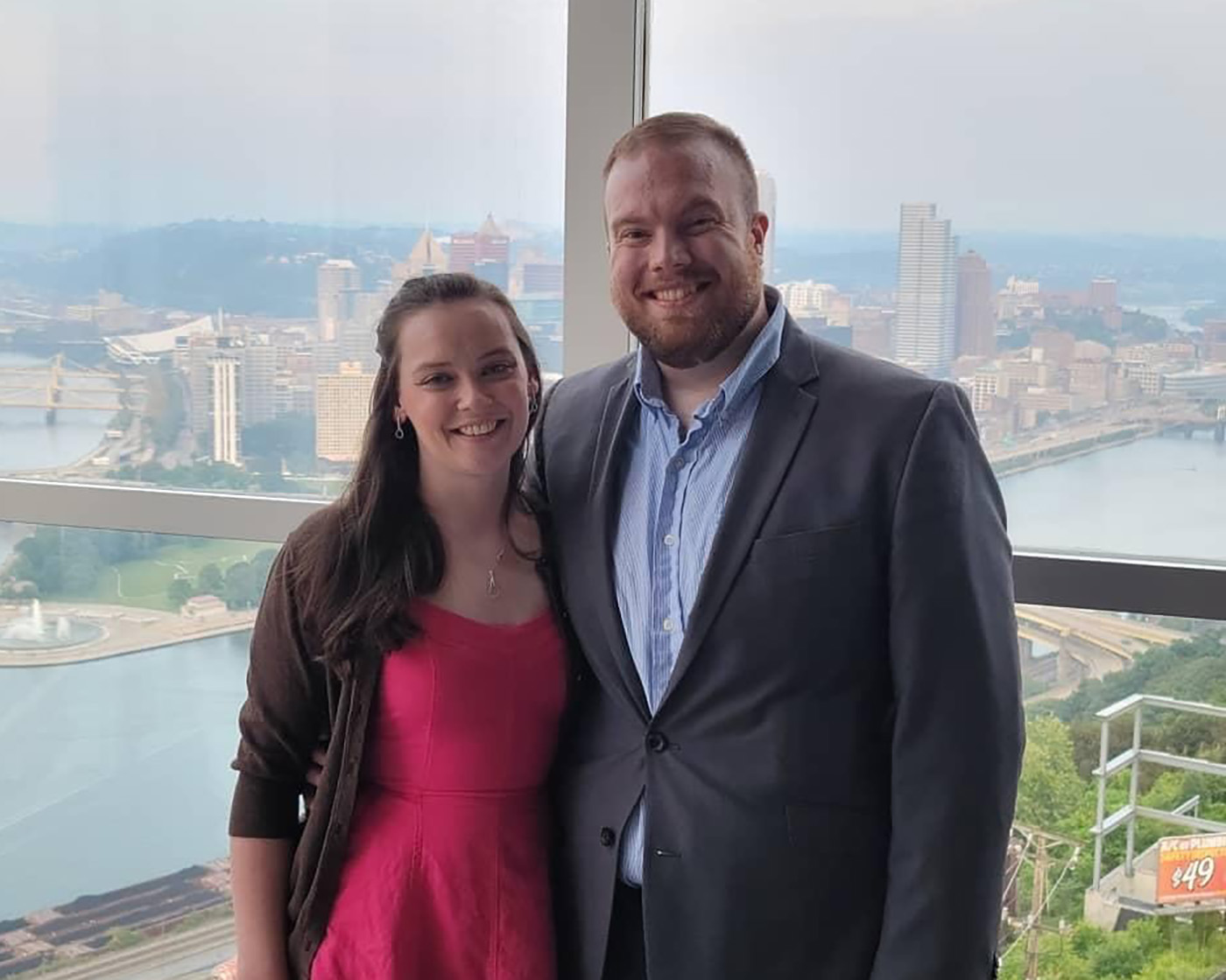 A man and woman stand in front of a window overlooking downtown Pittsburgh.