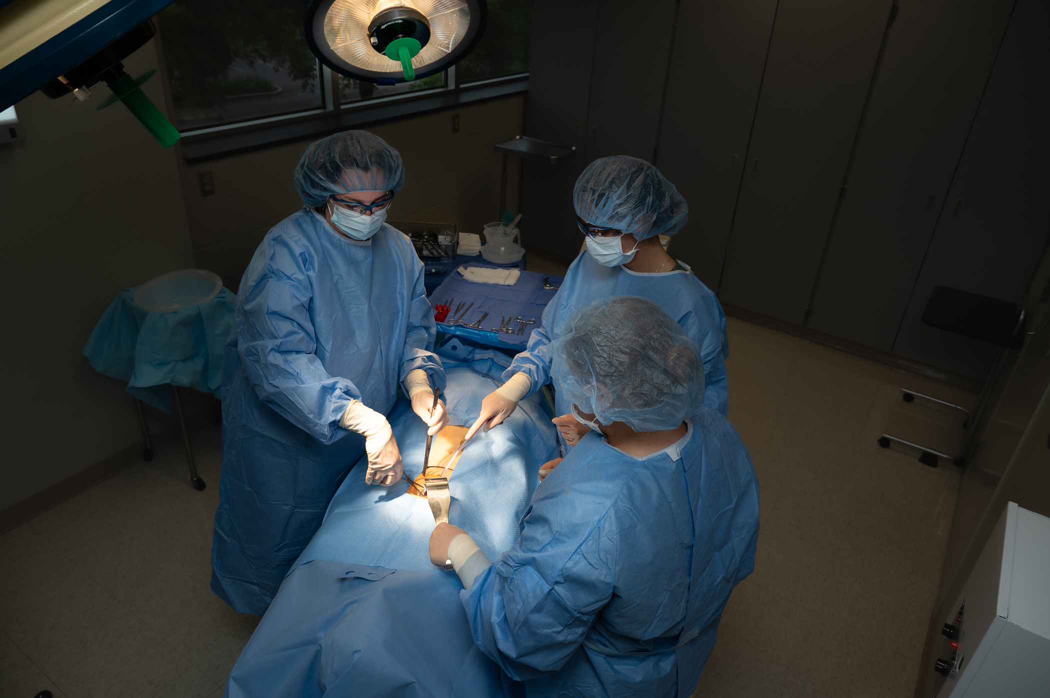 Two students in blue scrubs practice a mock operating room