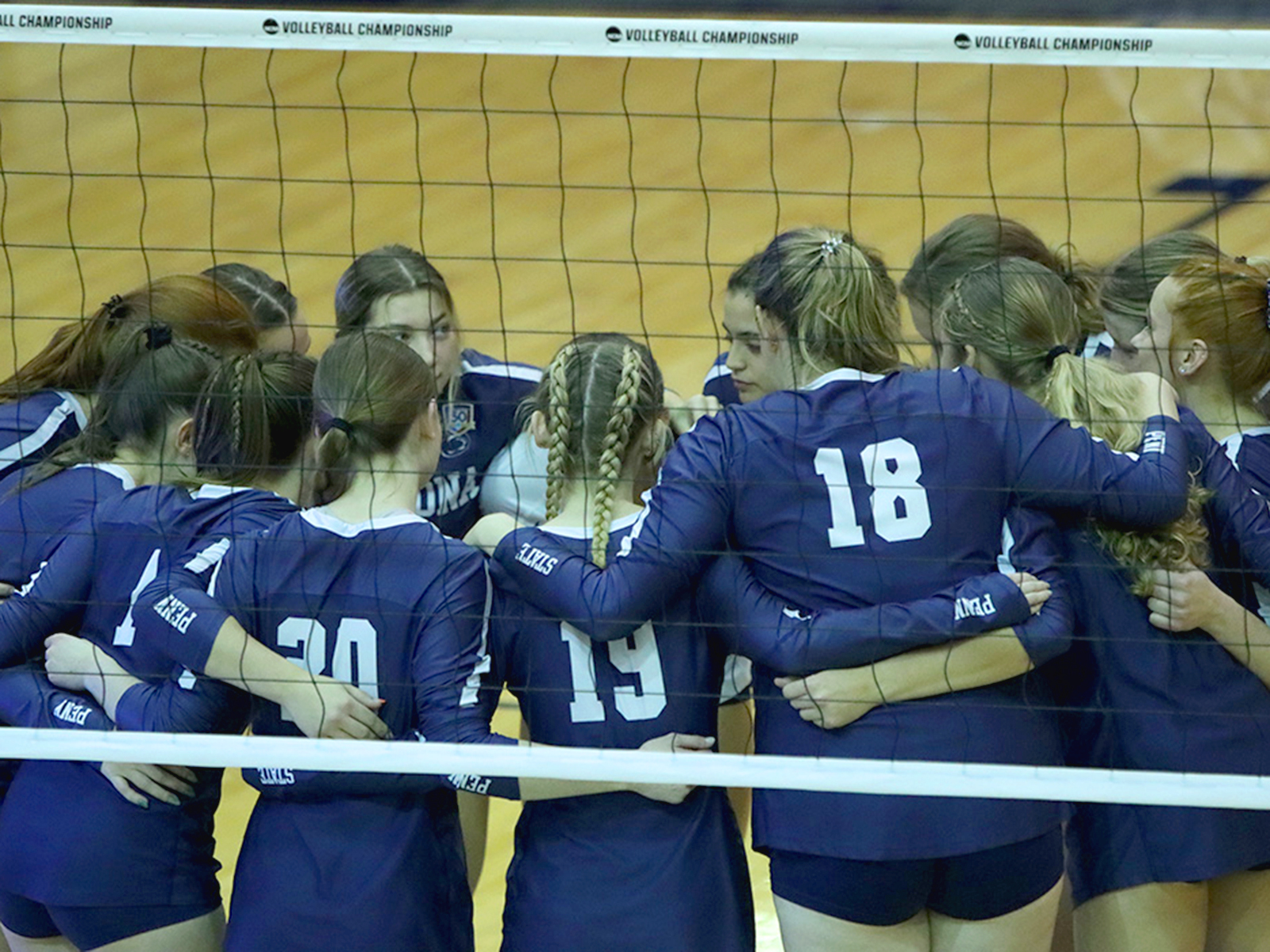 Penn State Altoona's 2023-24 women's volleyball team huddles before a game with a volleyball net in the foreground