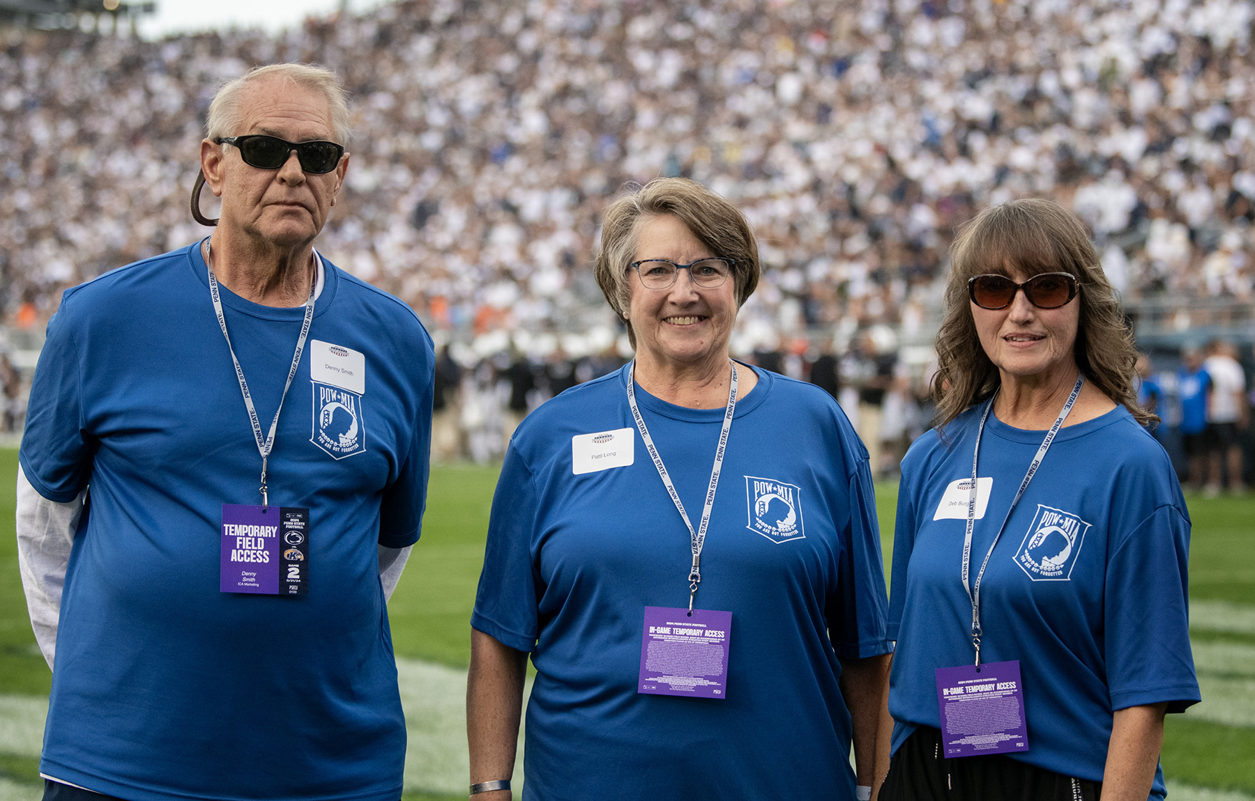 Three people stand on a football field in a crowded stadium.