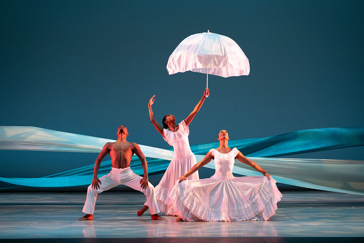 A trio of Black dancers look upward as they stand in rigid poses.