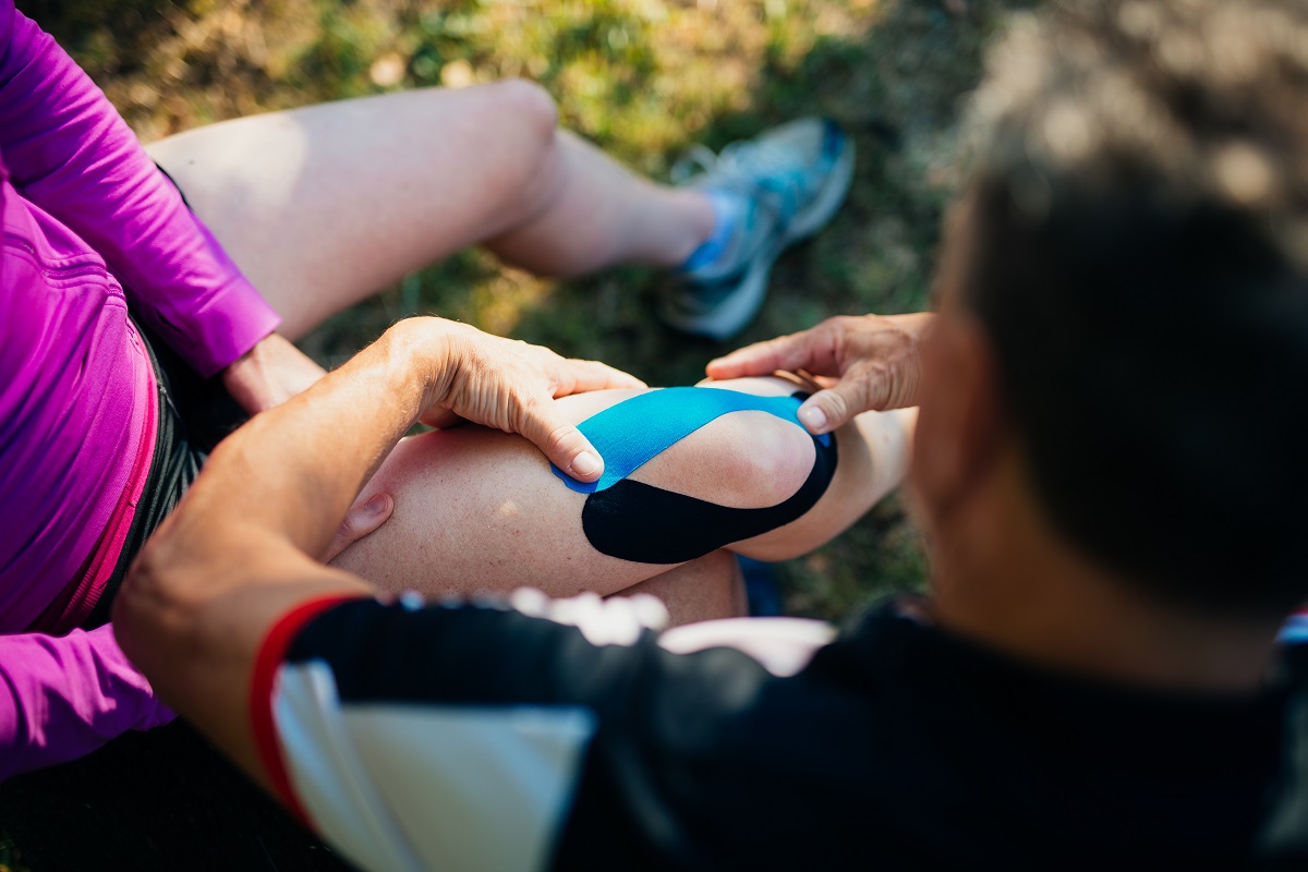 A man applies a bandage on knee of his wife.