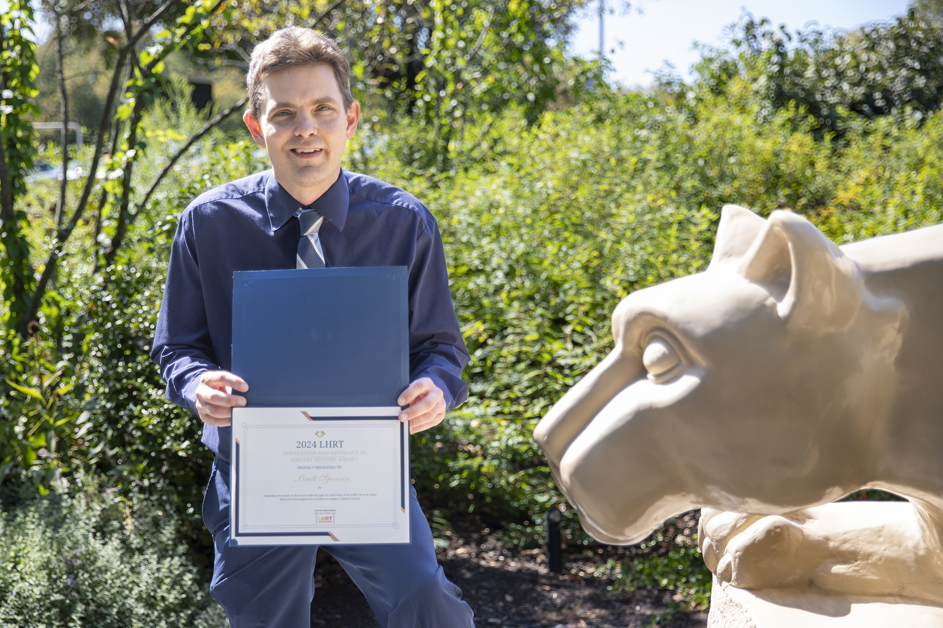 Brett Spencer holding award next to Nittany Lion statue