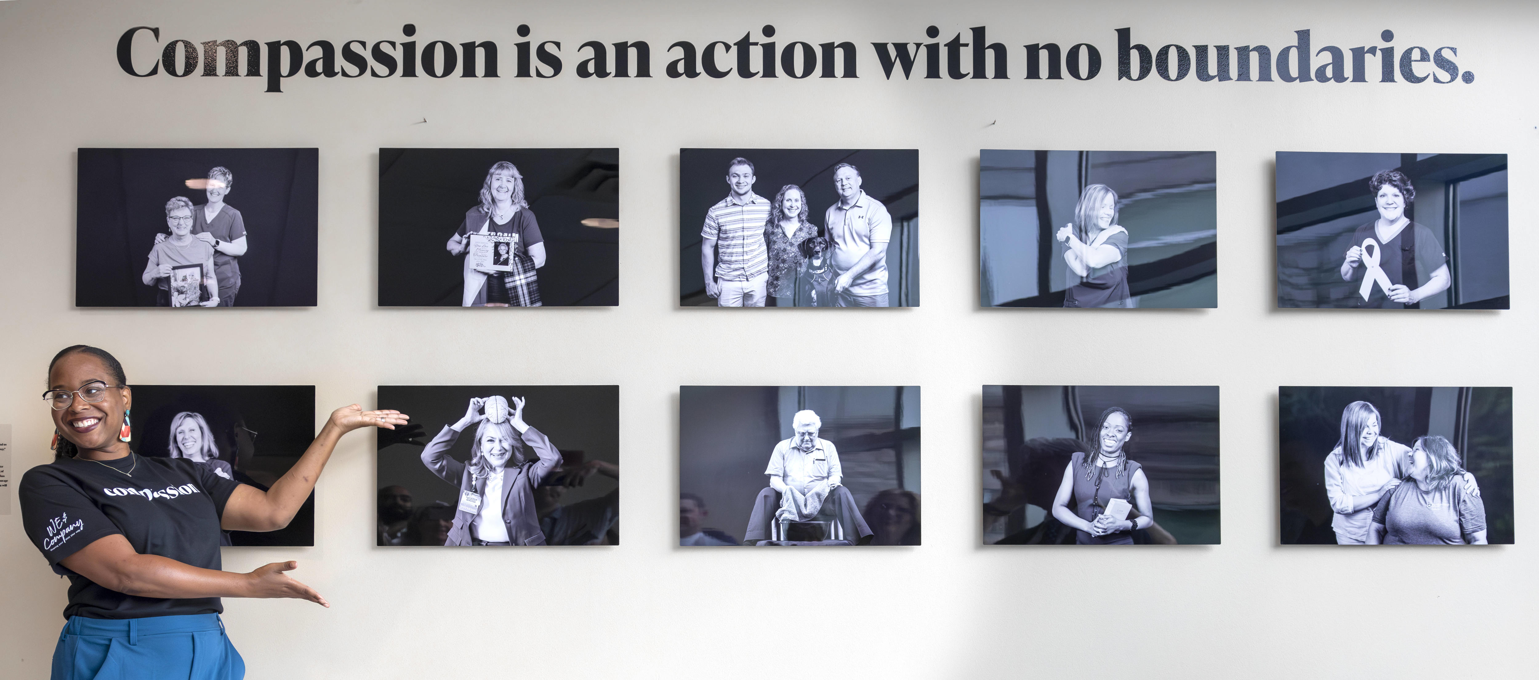 A woman stands with her arms partially outstretched, pointing toward and exhibit of 10 black and white photos on a wall.