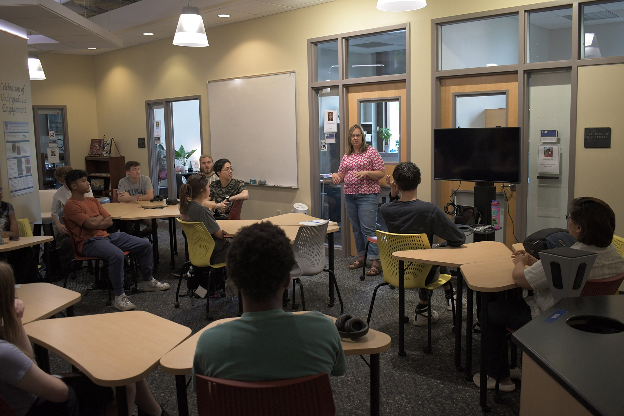 Person stands at the front of a room, talking to other people sitting at tables. 