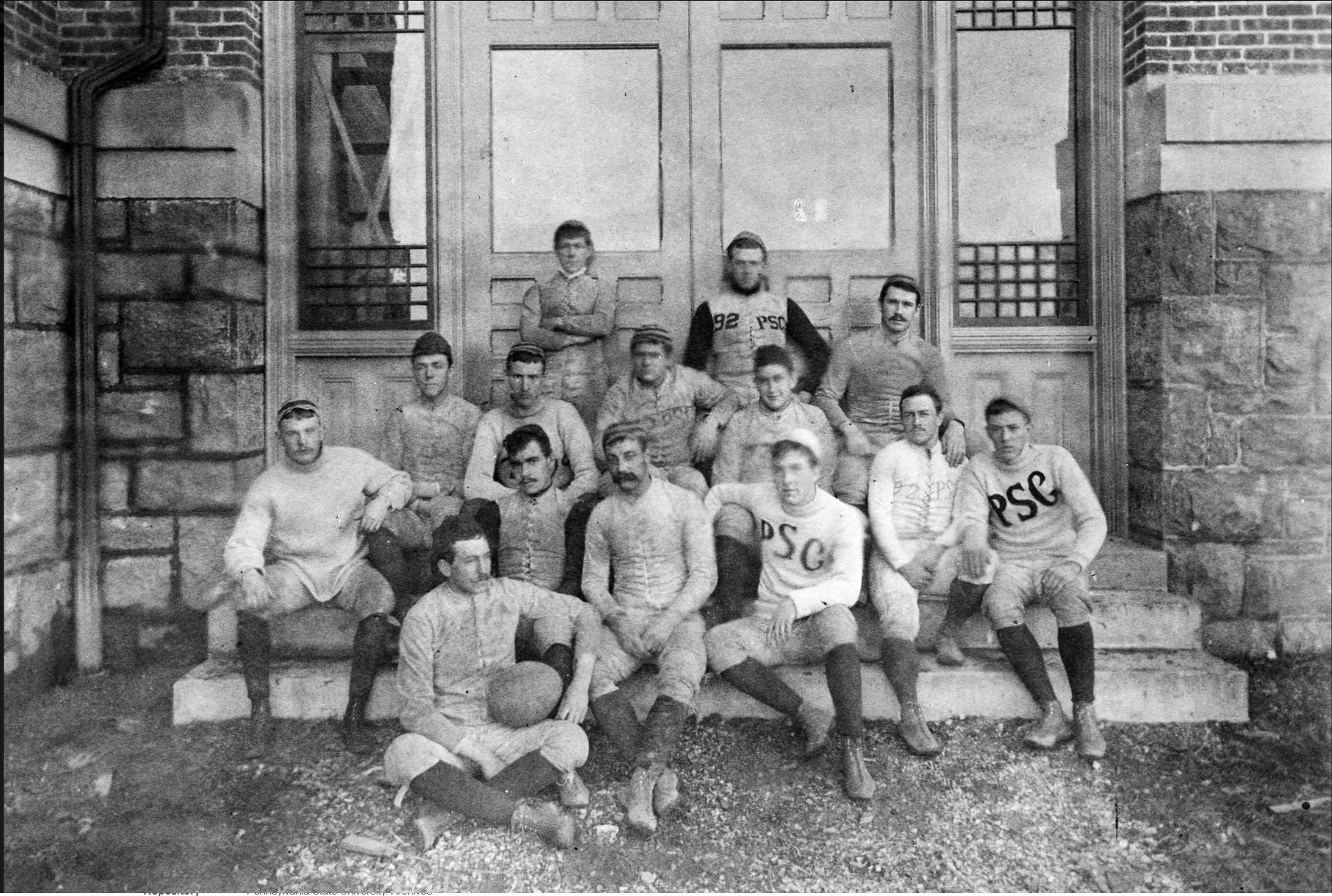 A photo of the football team, with most being seated on steps. The two in the back are leaning against a door.