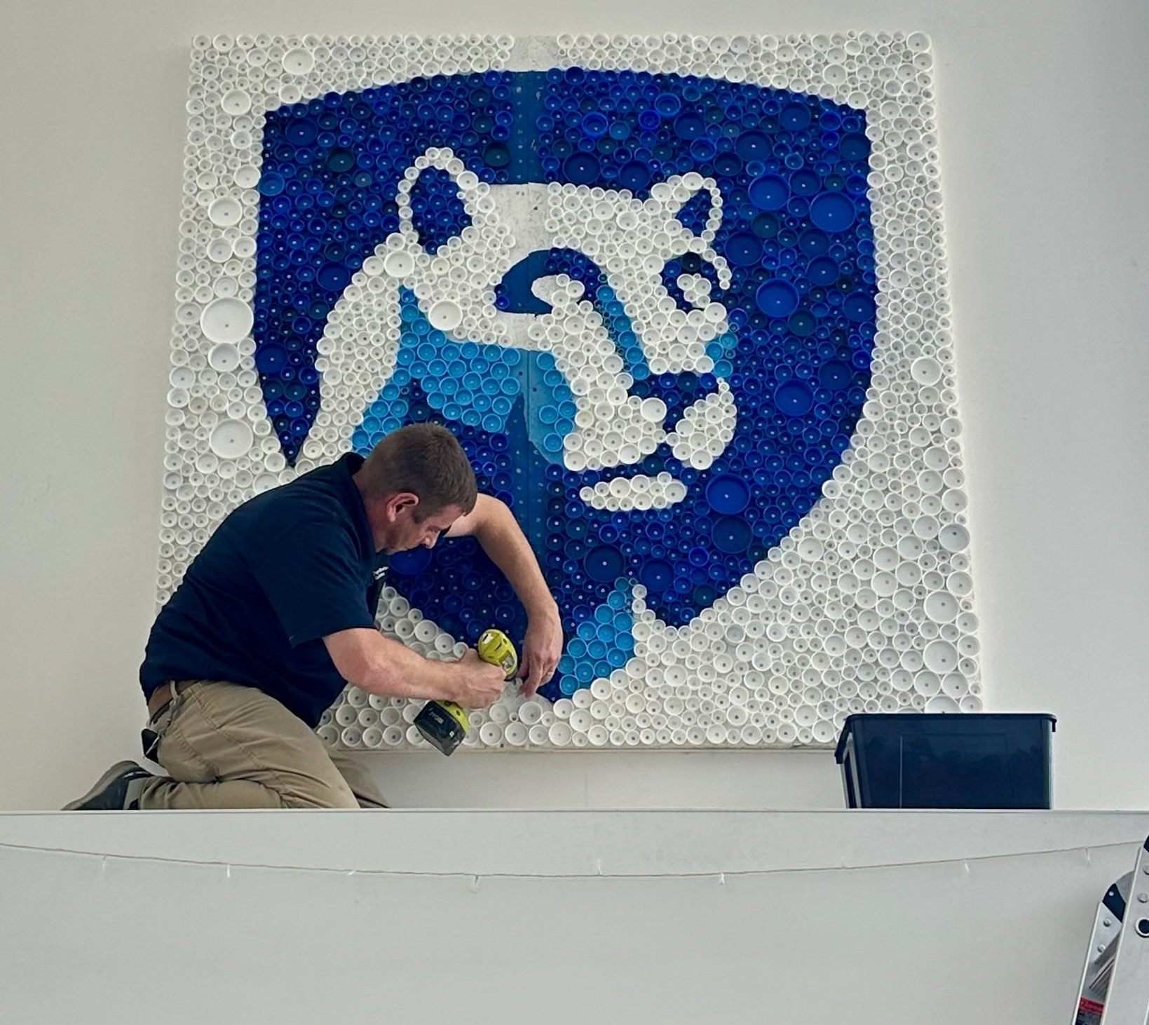 A person uses a drill to install a Nittany Lion mural