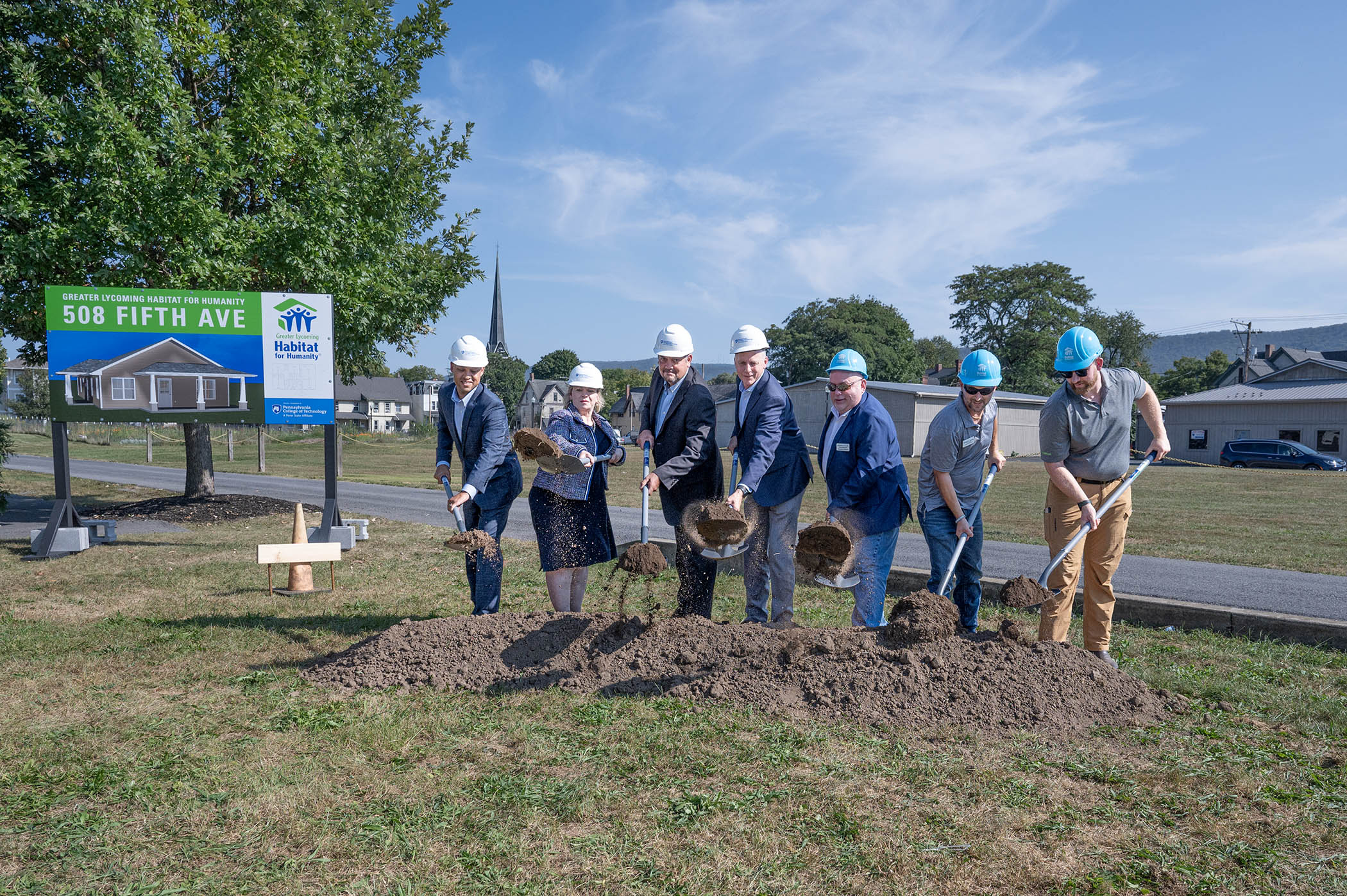 A group of people with shovels participate in an outside groudbreaking ceremony on a beautiful summer day