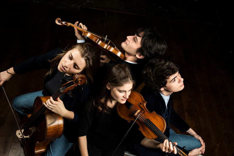 Four white musicians hold their string instruments in a bird's-eye view photo.