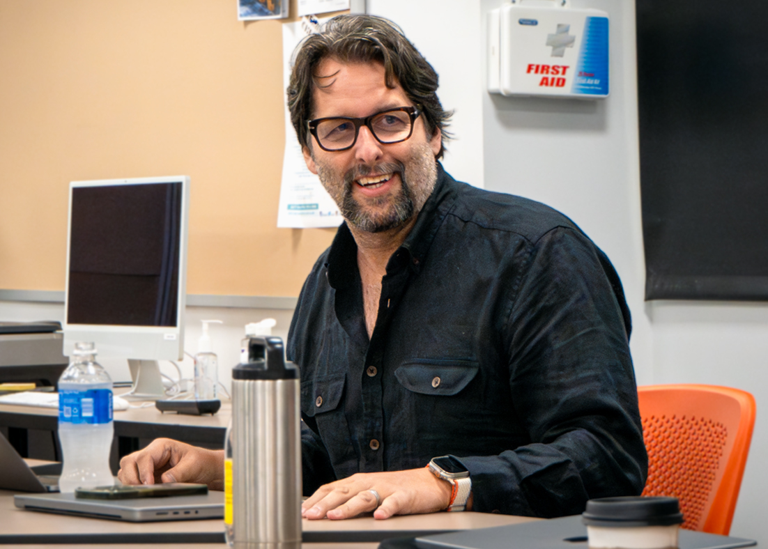 Michael McIntyre sits in a classroom while engaging with students. 