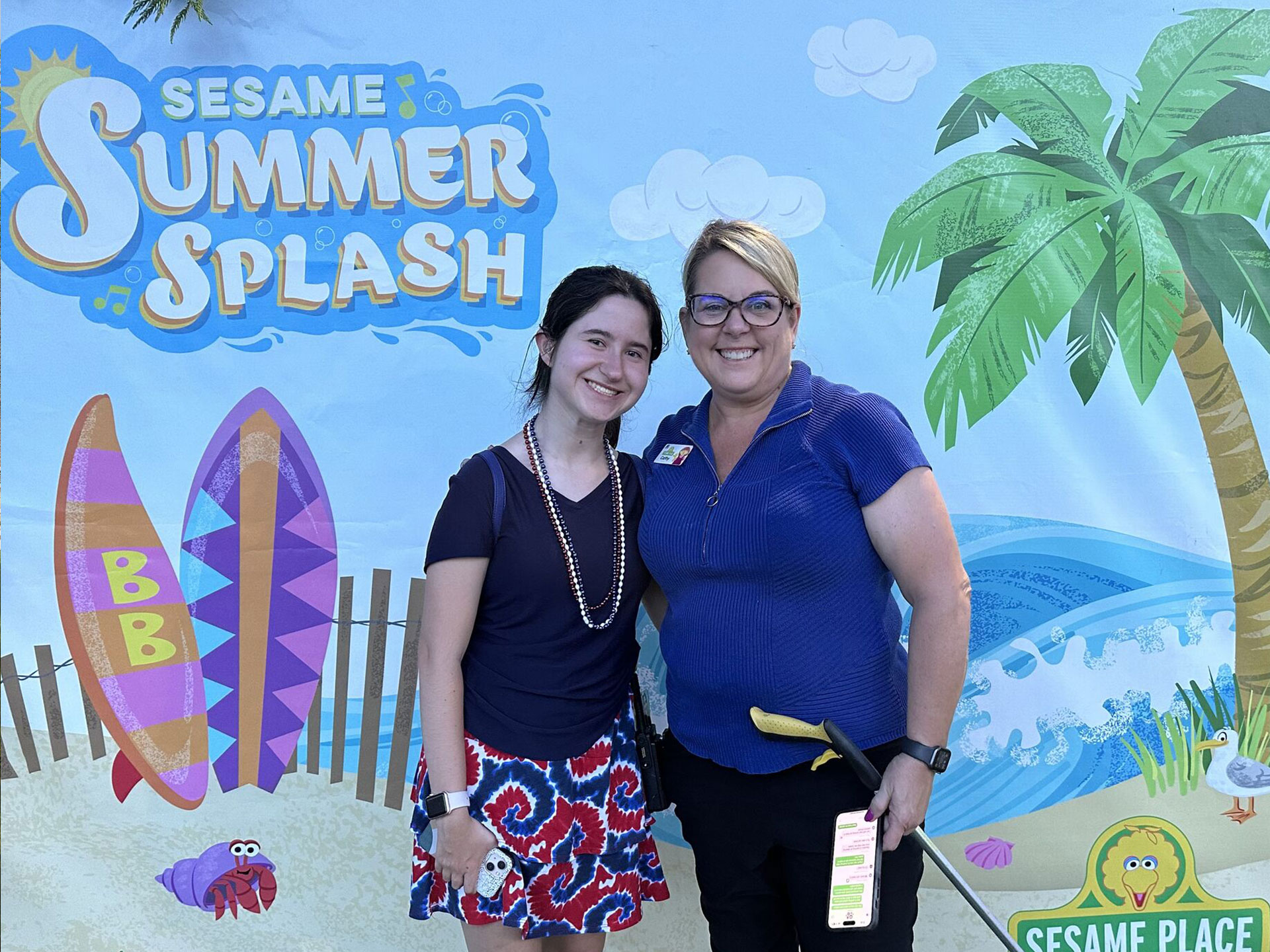 Two women standing in front of a Sesame Place sign