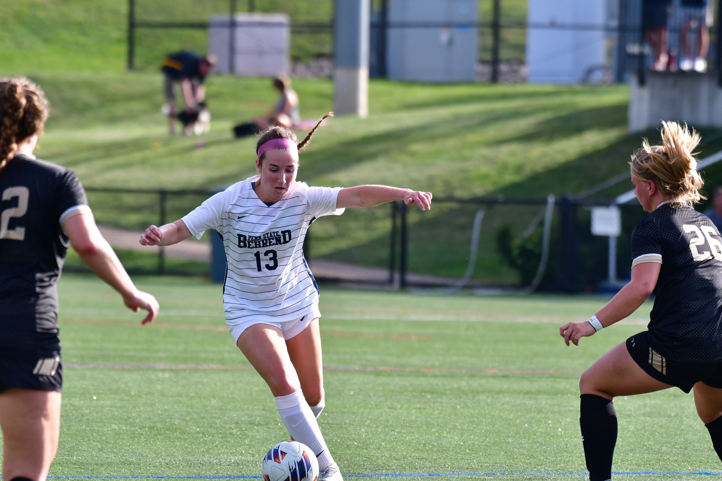 A Penn State Behrend soccer player dribbles between two defenders.