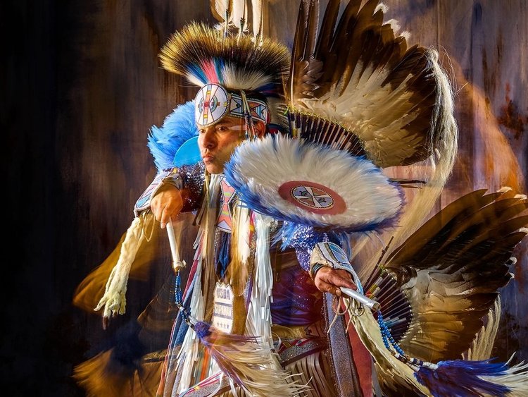 An indigenous man wears Native American tribal regalia in a stylized portrait.