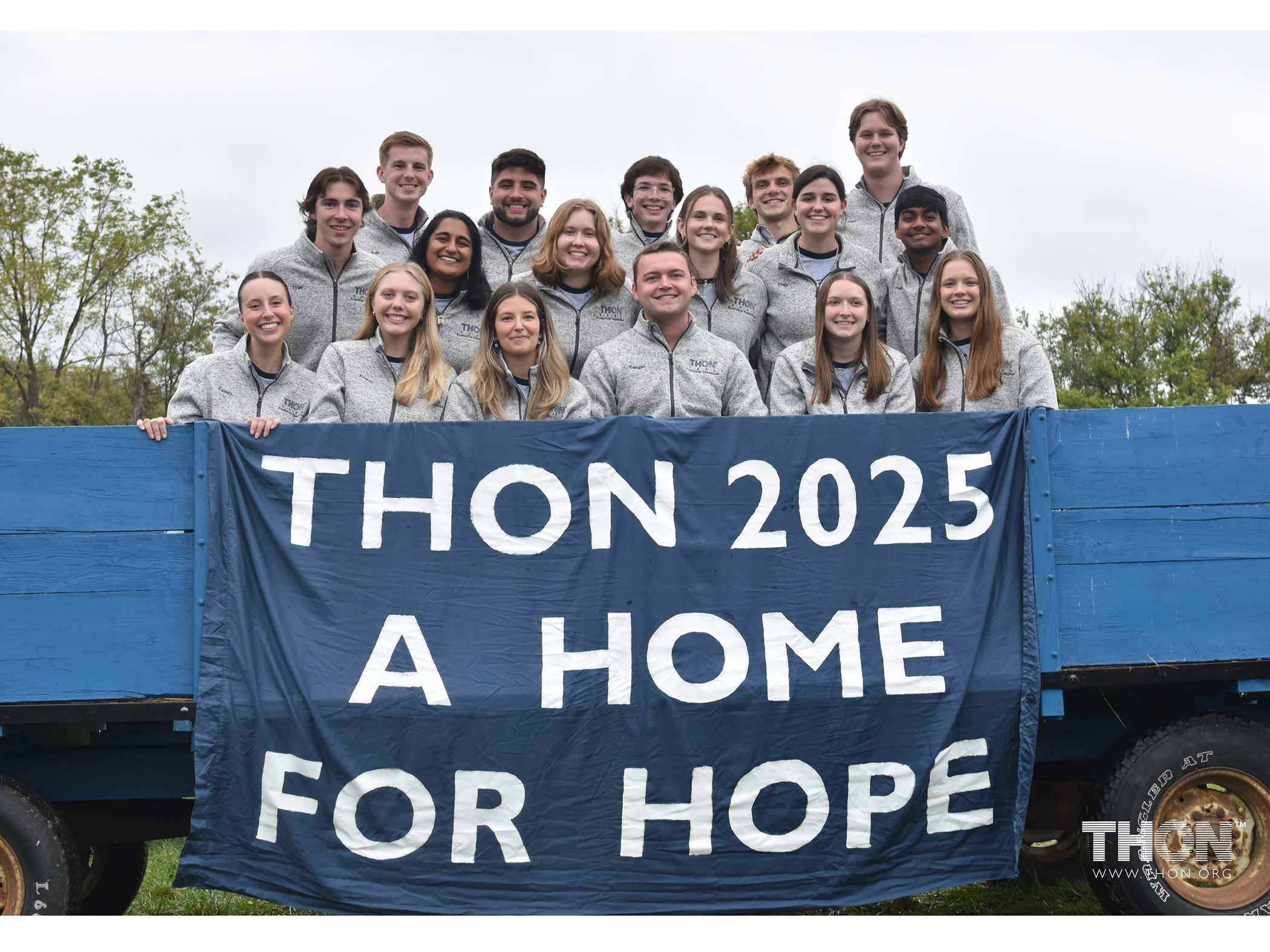 A group of students standing in the bed of a blue wagon with a sign reading Thon 2025 a home for hope