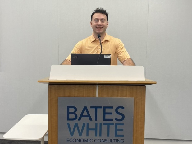 Colin Byrne stands behind a podium that reads Bates White Economic Consulting on the front.