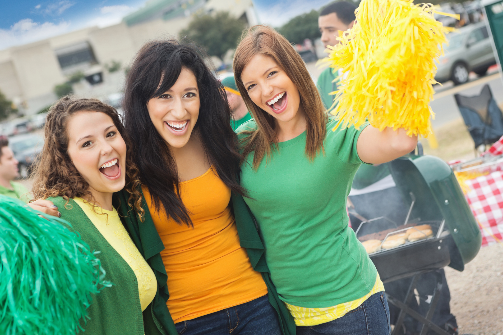 Three young people outside a sporting event wearing team colors and holding pom poms