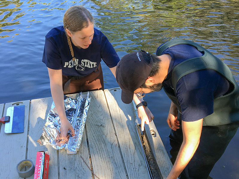 Two people standing in the water by a dock examining a dirt core from the ground